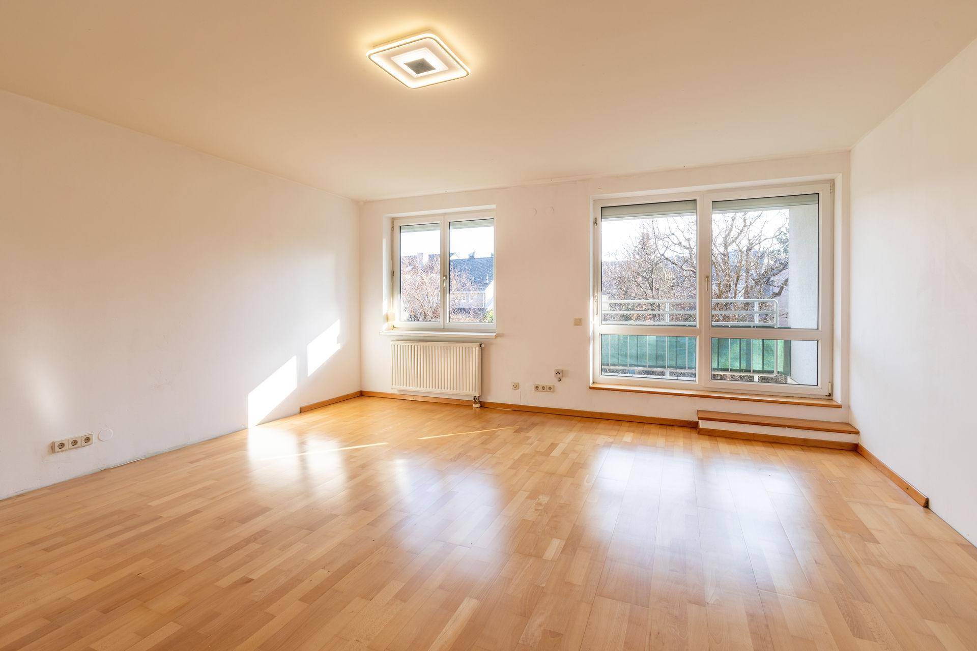 Lichtdurchflutetes Zimmer mit Parkettboden und großen Fenstern, ideal für Wohn- oder Schlafbereich.