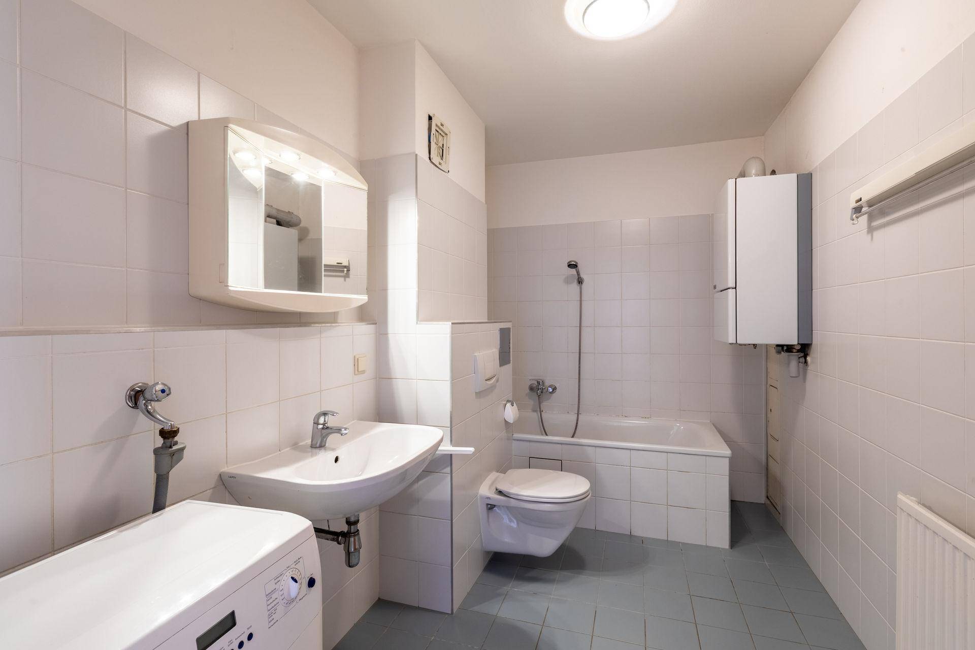 Helles Badezimmer mit Badewanne, Waschbecken, WC und Waschmaschine, komplett gefliest.