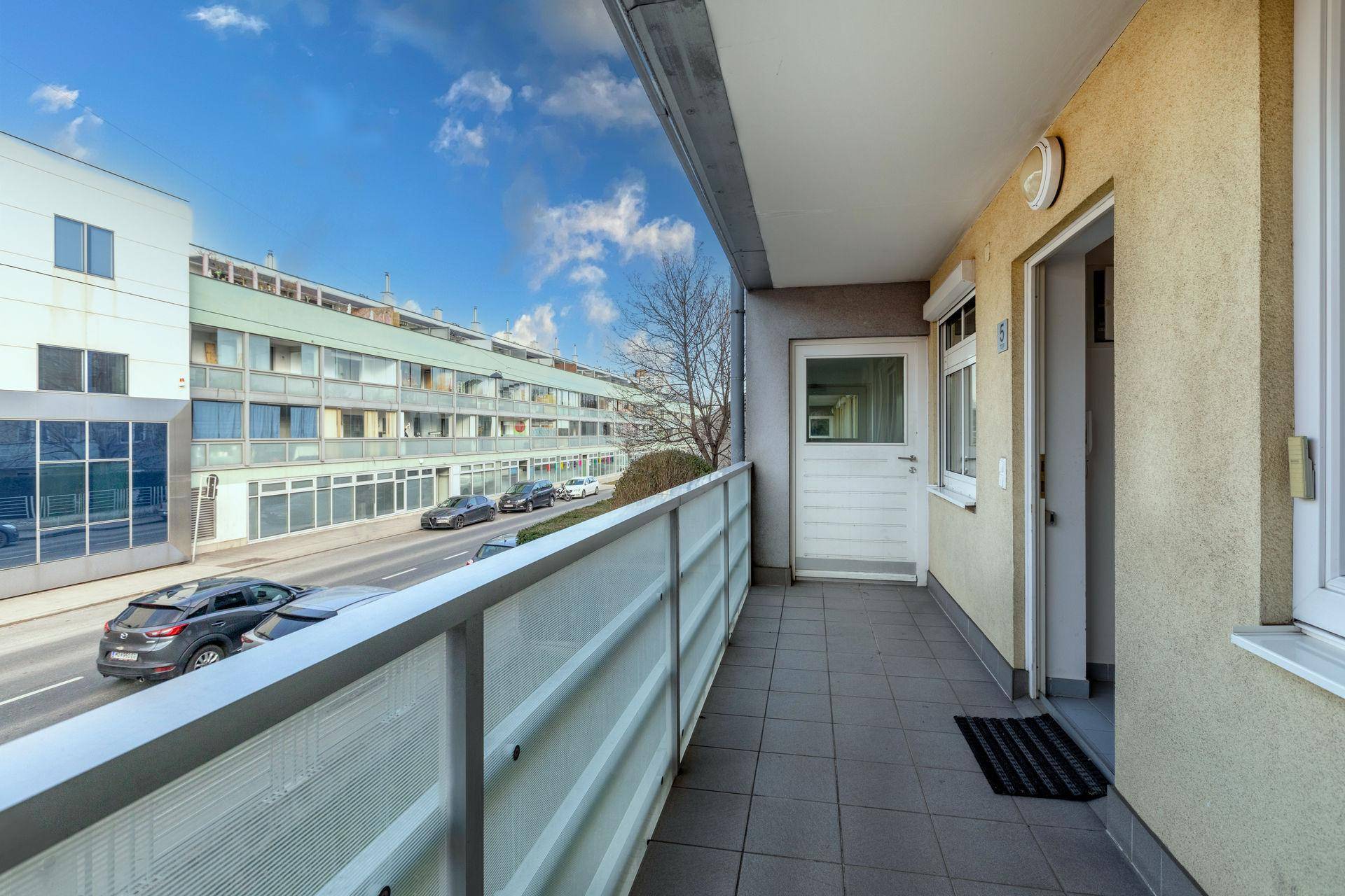 Langer Balkon mit Fliesenboden und Blick auf die Straße und gegenüberliegende Gebäude.