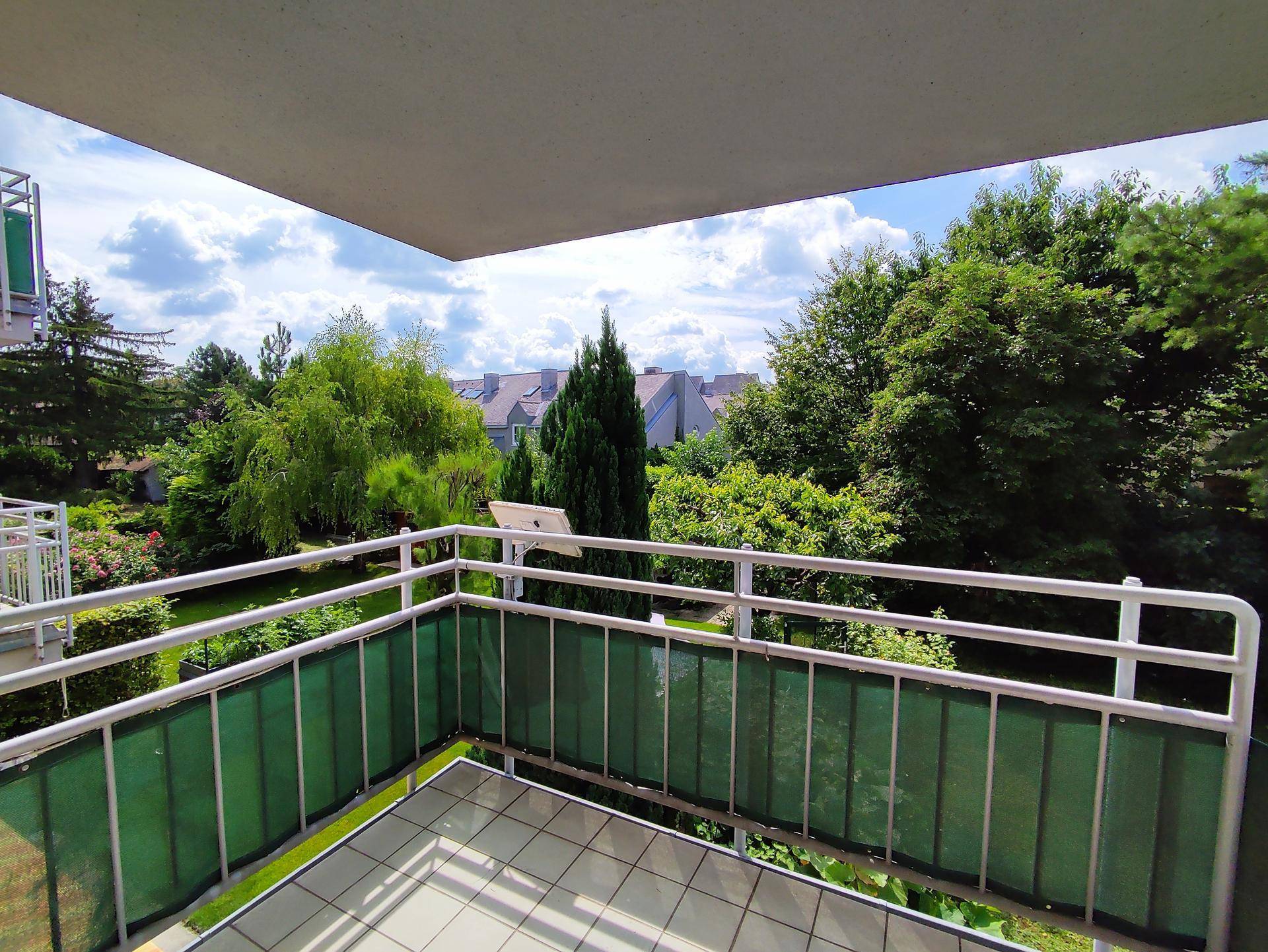 Balkon mit grüner Umzäunung und Blick auf den begrünten Innenhof und umliegende Häuser.
