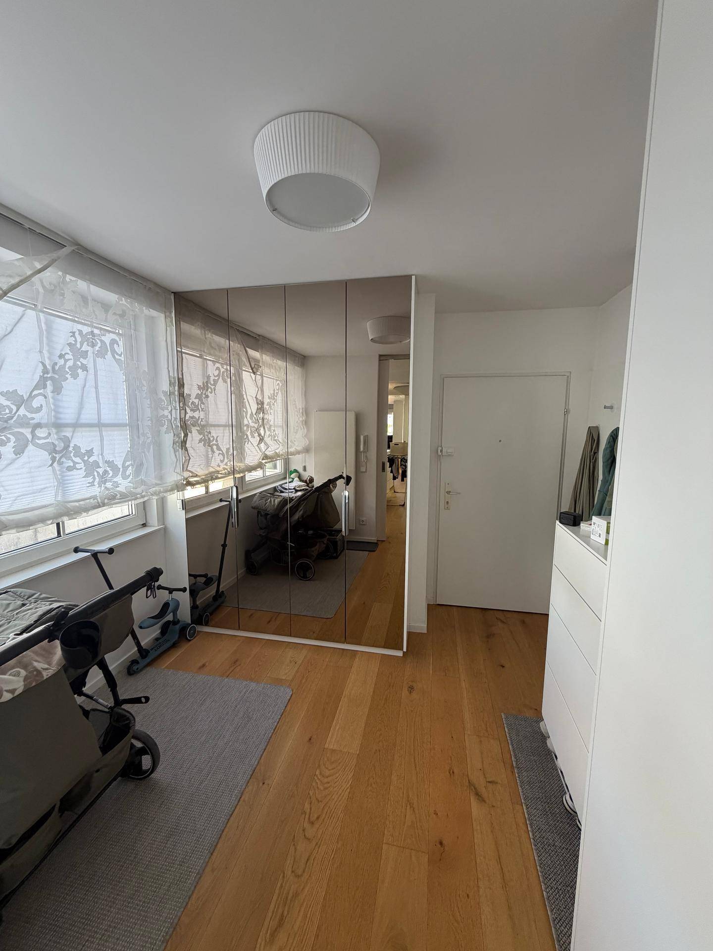 Eingangsbereich mit Spiegelschränken, Holzboden und Fenster, das den Raum erhellt.