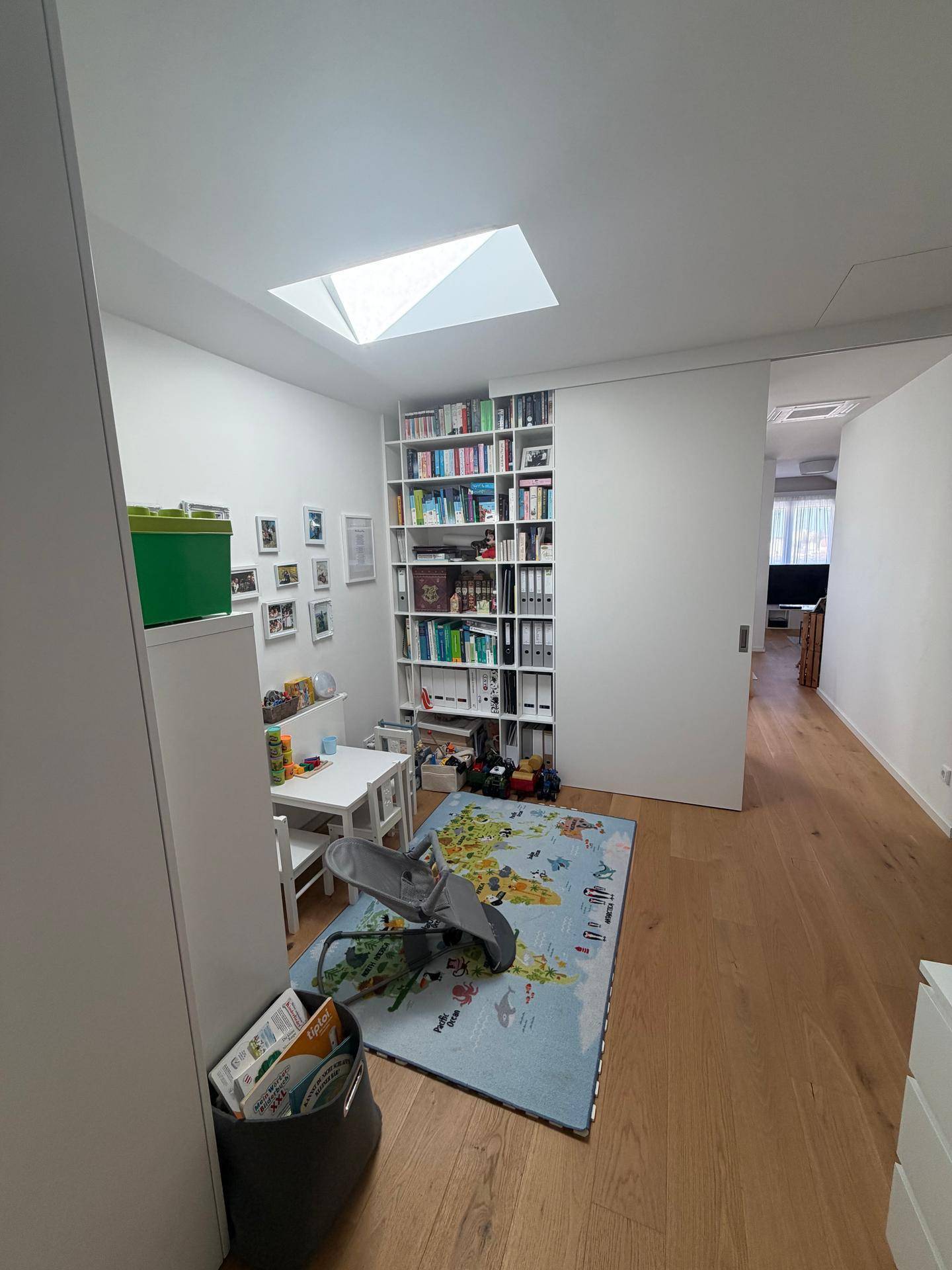 Helles Kinderzimmer mit Bücherregal, Spielbereich und Dachfenster für viel Tageslicht.