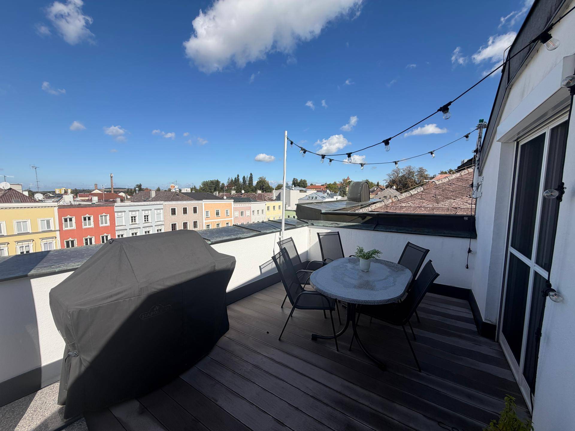Geräumige Dachterrasse mit Esstisch, Grill und Lichterkette, ideal für gesellige Abende mit Stadtblick.