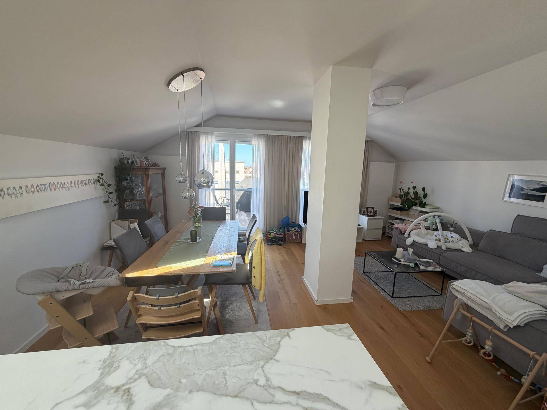 Heller offener Wohn-Essbereich mit Holzboden, modernem Esstisch und Zugang zu einem Balkon.