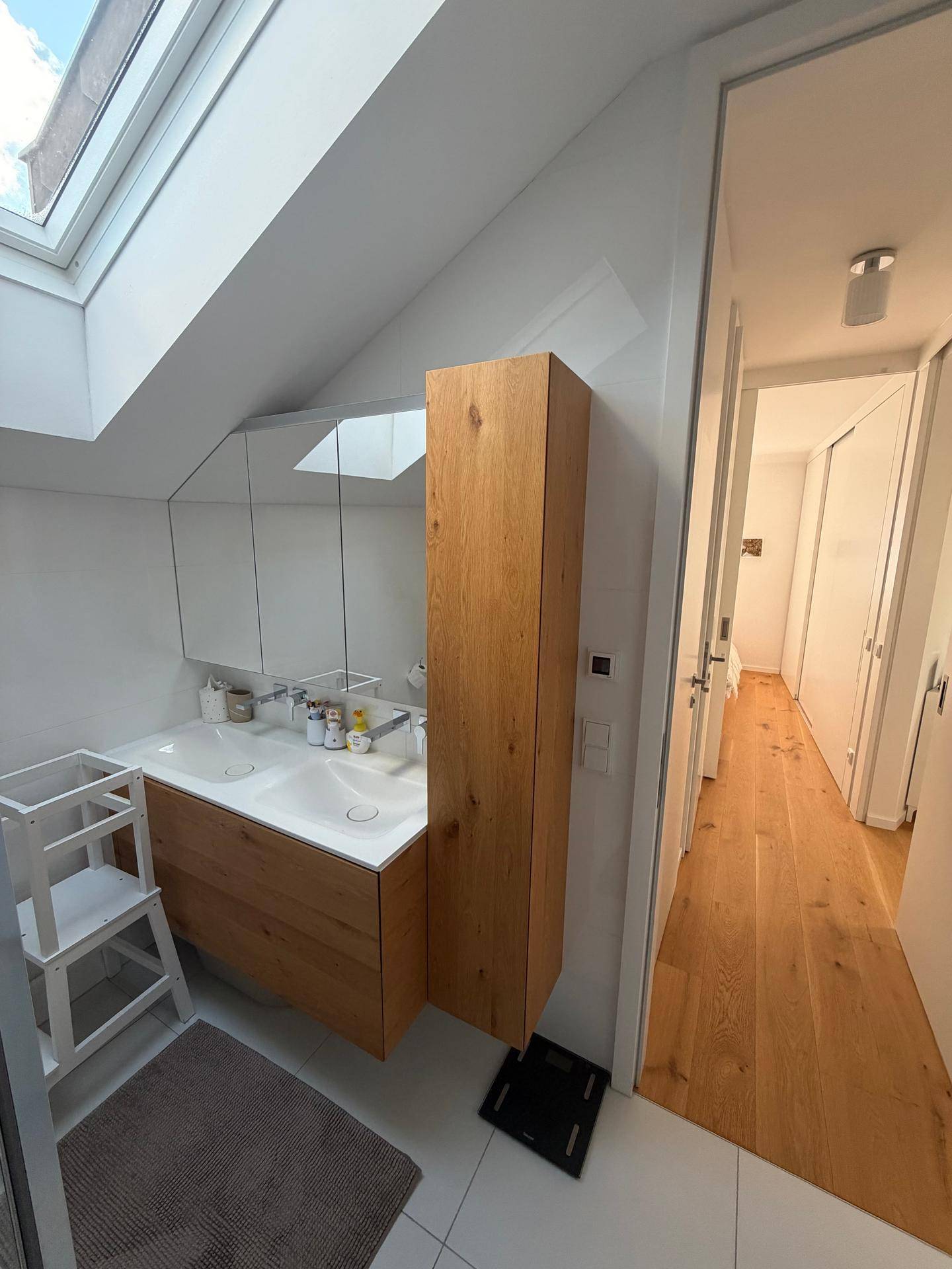 Modernes Badezimmer mit Doppelwaschbecken, Holzschrank und Dachfenster, das den Raum erhellt.