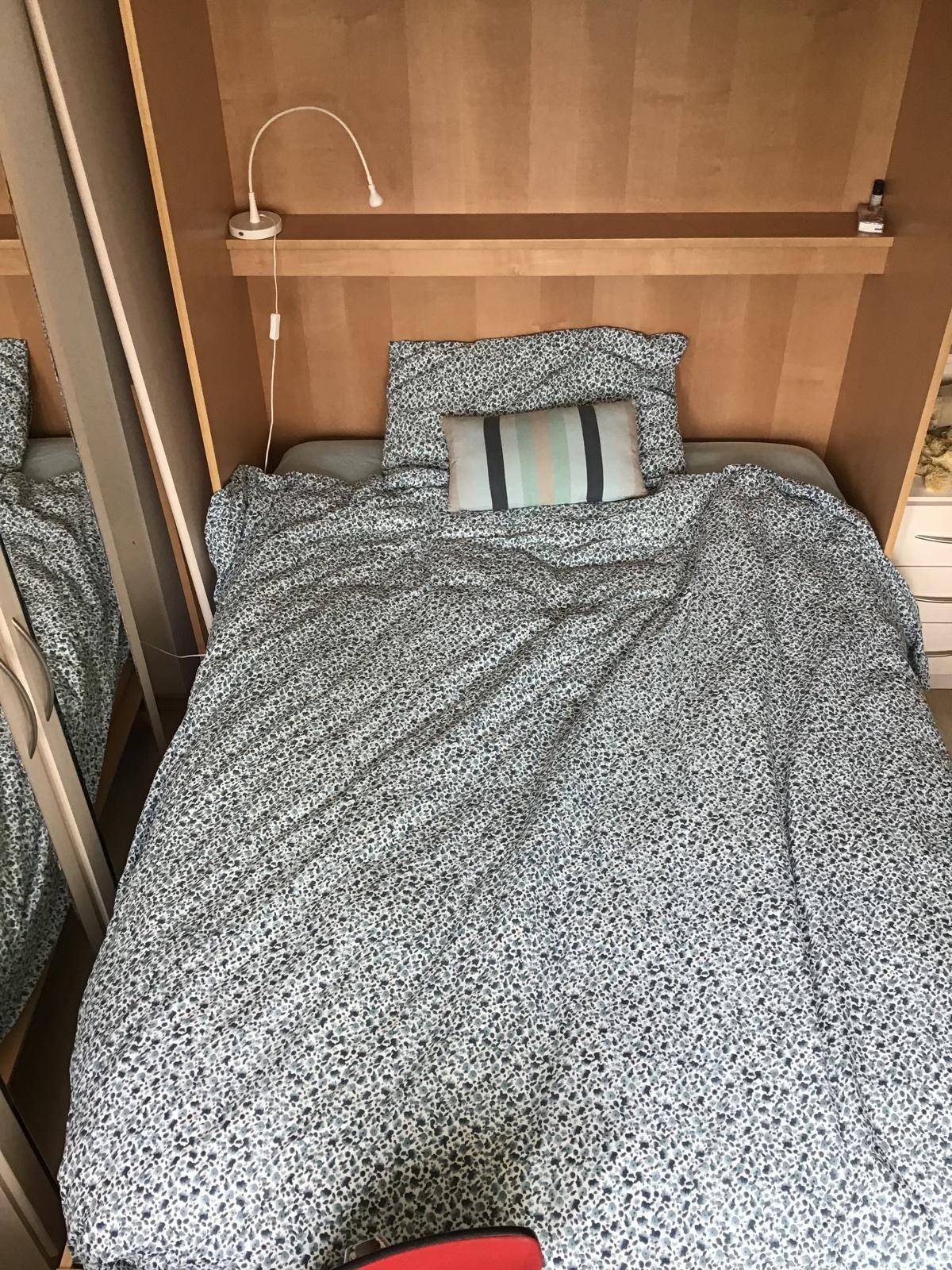 Gemütliches Bett mit gemusterter Bettwäsche und integriertem Kopfteil mit Leselampe.