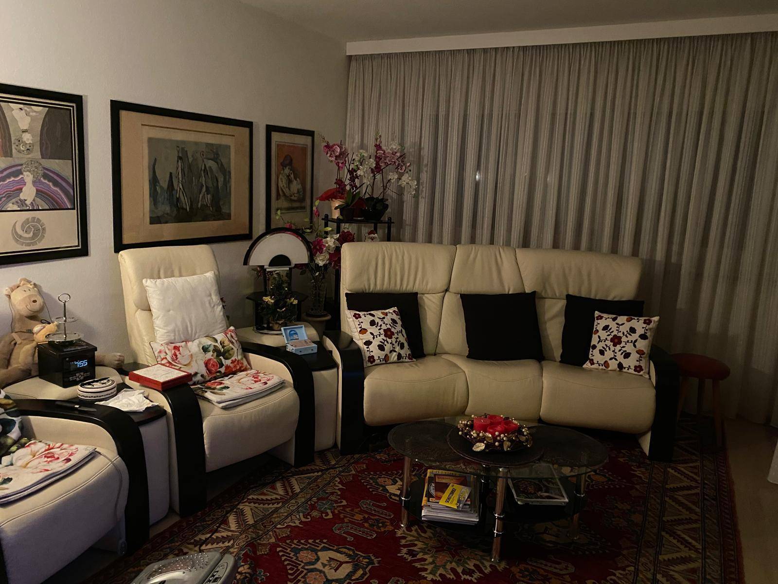Wohnzimmer mit beigem Sofa, Sesseln und einem gemusterten Teppich, dekoriert mit vielen Bildern.