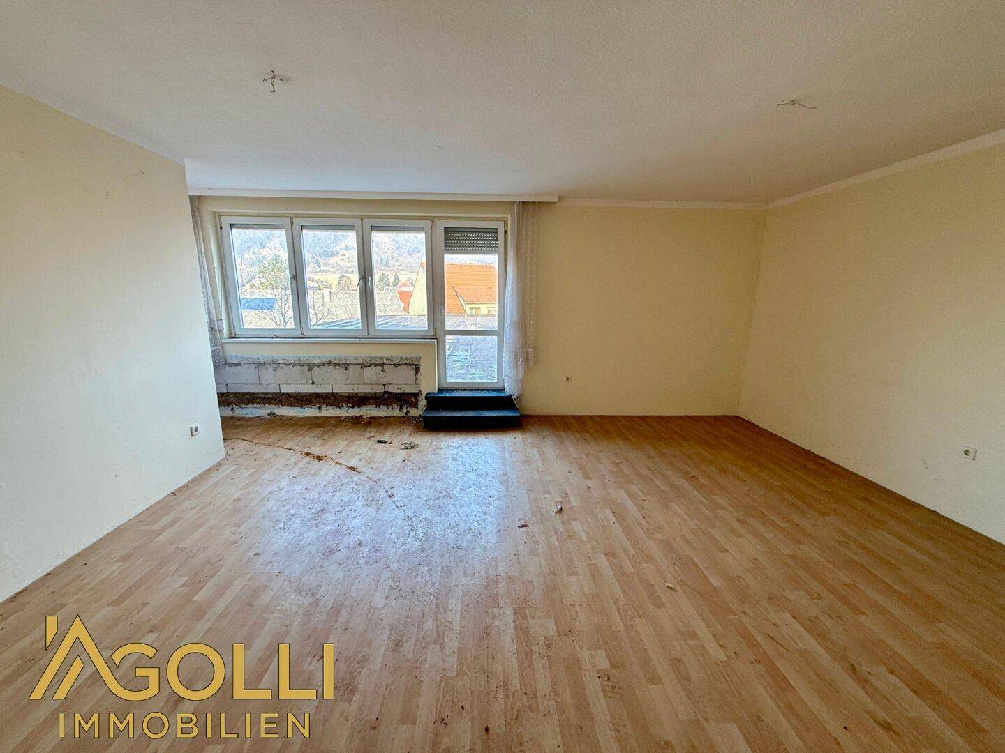 Geräumiger Innenraum mit Laminatboden und großen Fenstern, bereit für eine umfassende Renovierung.