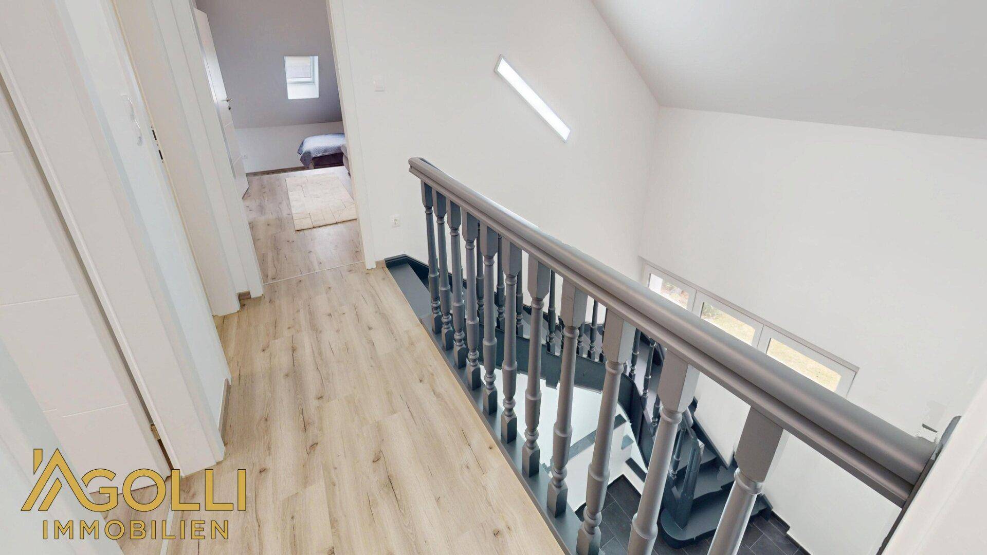Heller Flur im Obergeschoss mit Holzoptik-Laminatboden und Treppenaufgang.