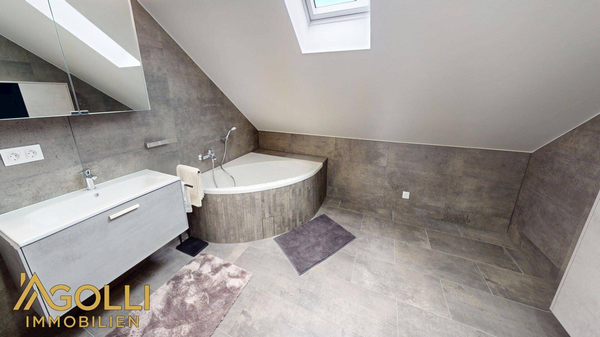 Modernes Badezimmer im Dachgeschoss mit Eckbadewanne, Waschbecken und Dachfenster.