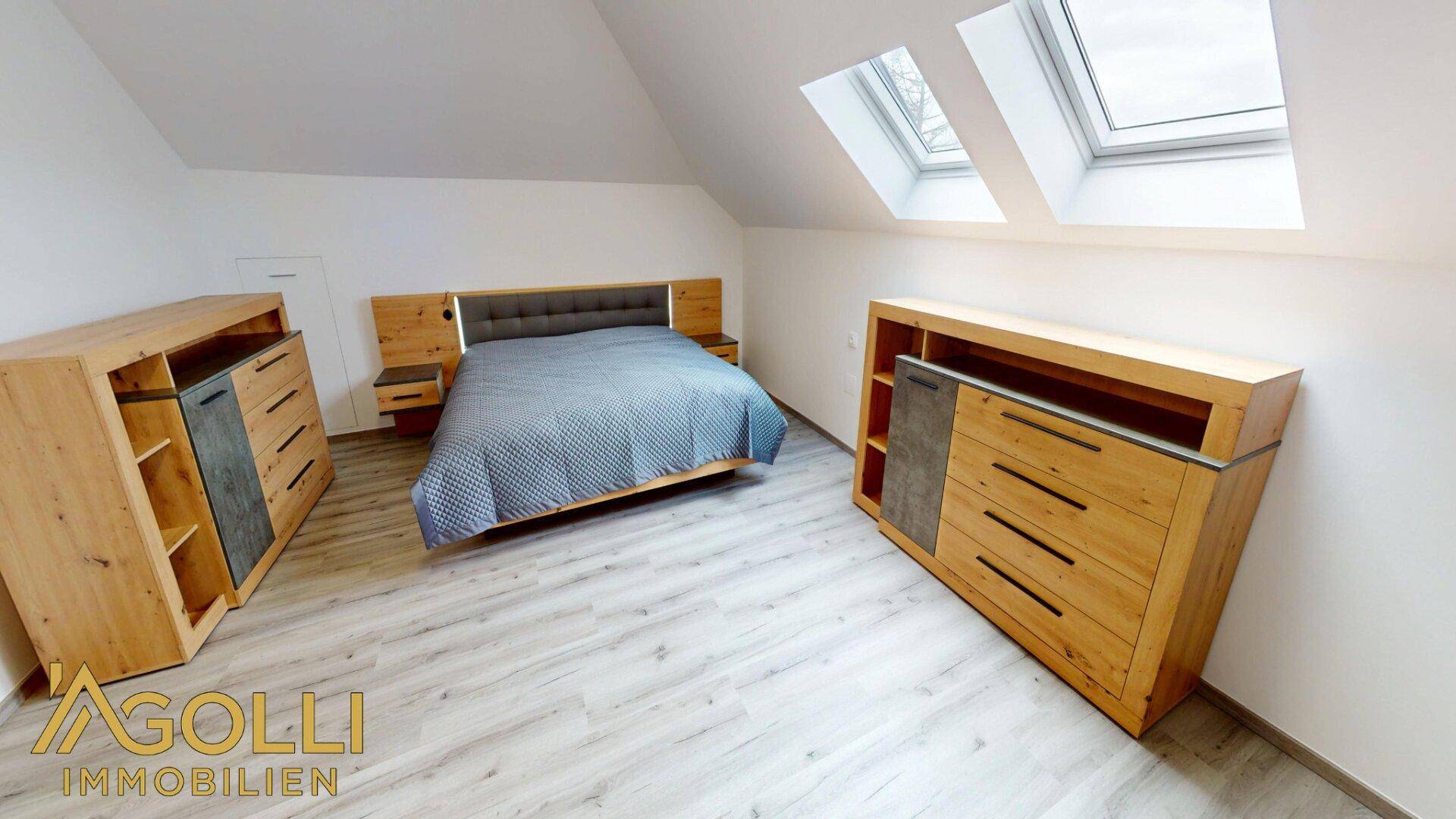 Geräumiges Schlafzimmer im Dachgeschoss mit Holzmöbeln und Dachfenstern.