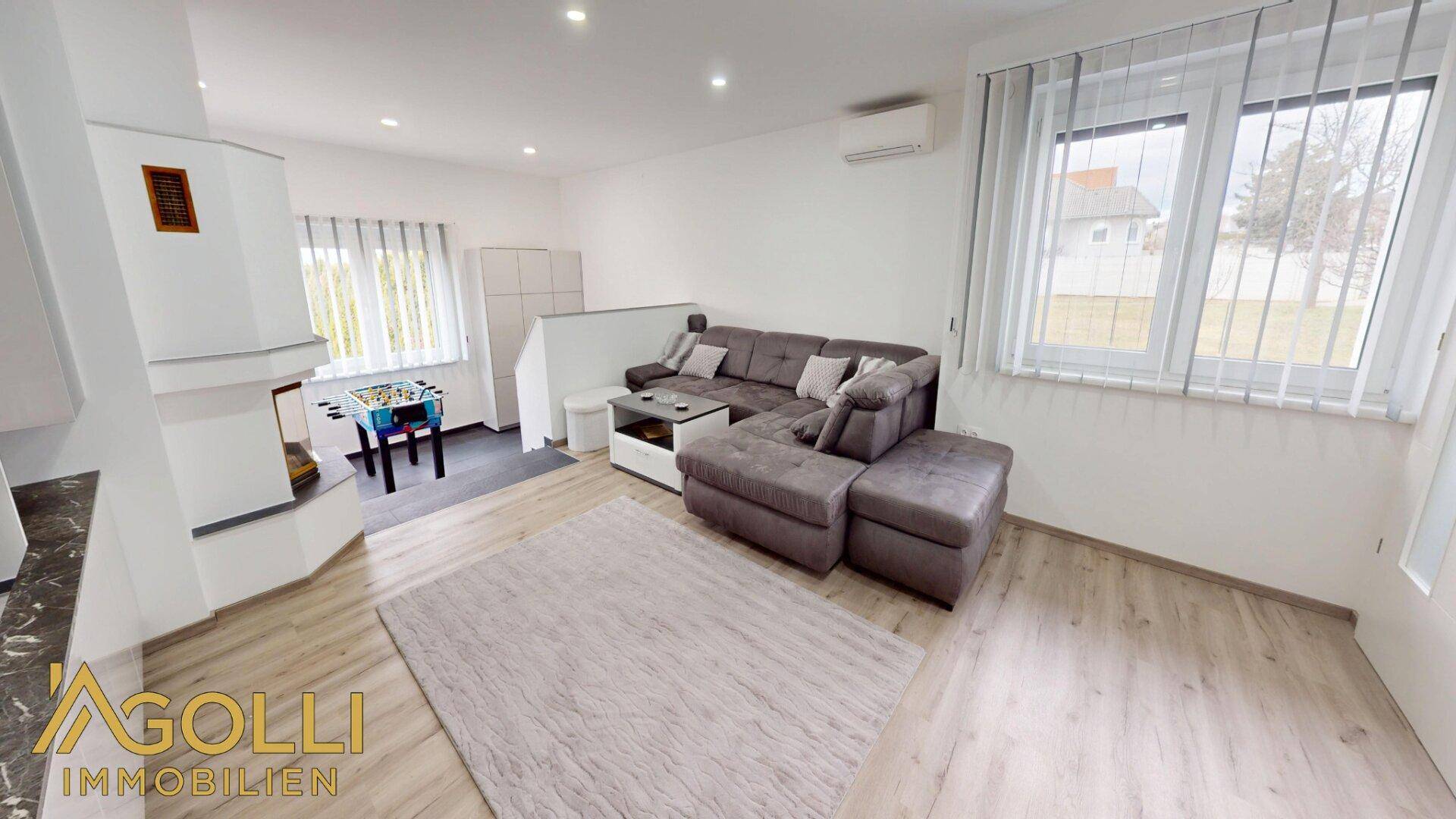 Helles Wohnzimmer mit großem Sofa, Laminatboden und Fenstern mit Blick ins Grüne.