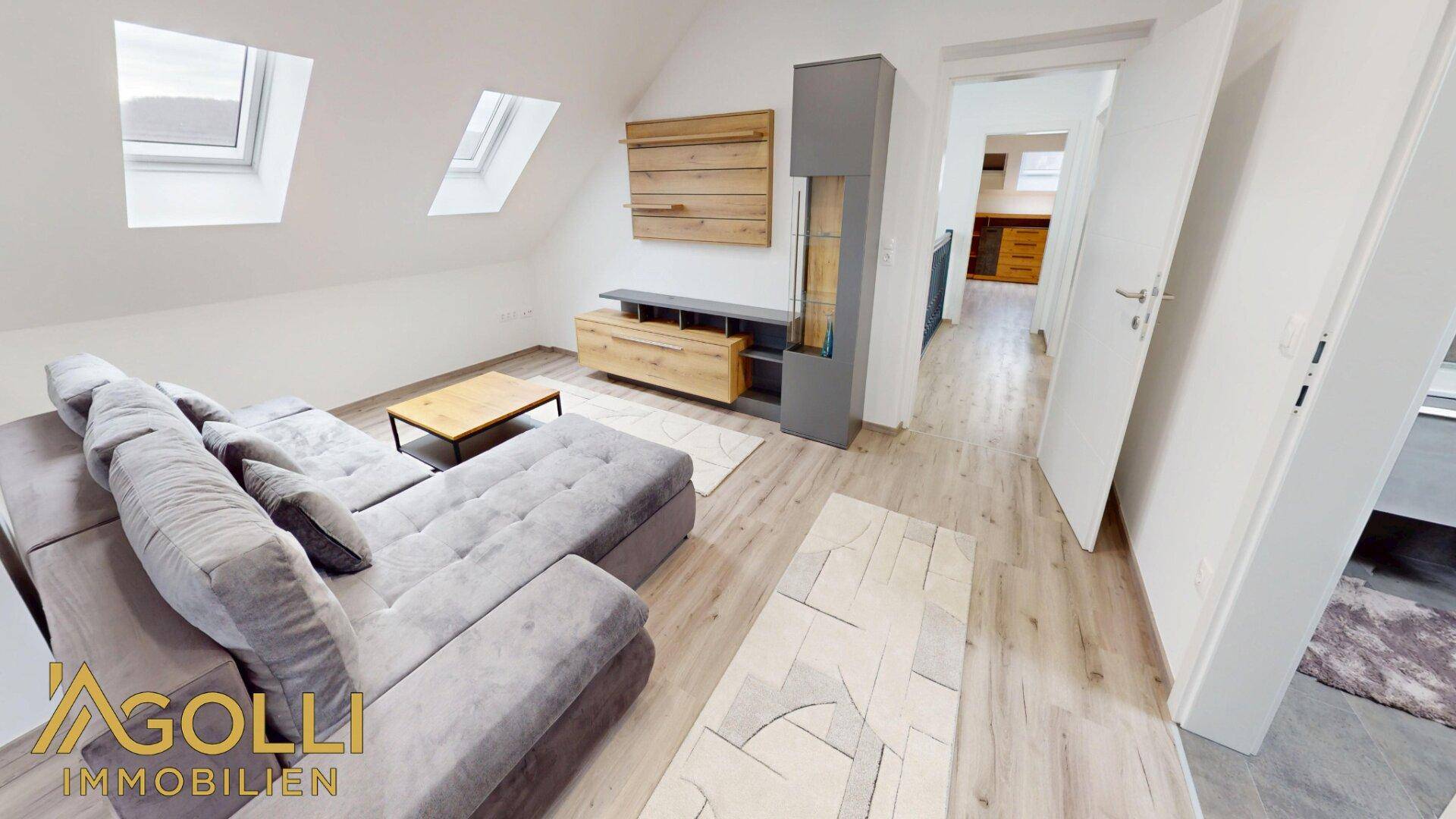 Gemütlicher Wohnbereich im Dachgeschoss mit Schrägdach, Dachfenstern und modernem Sofa.