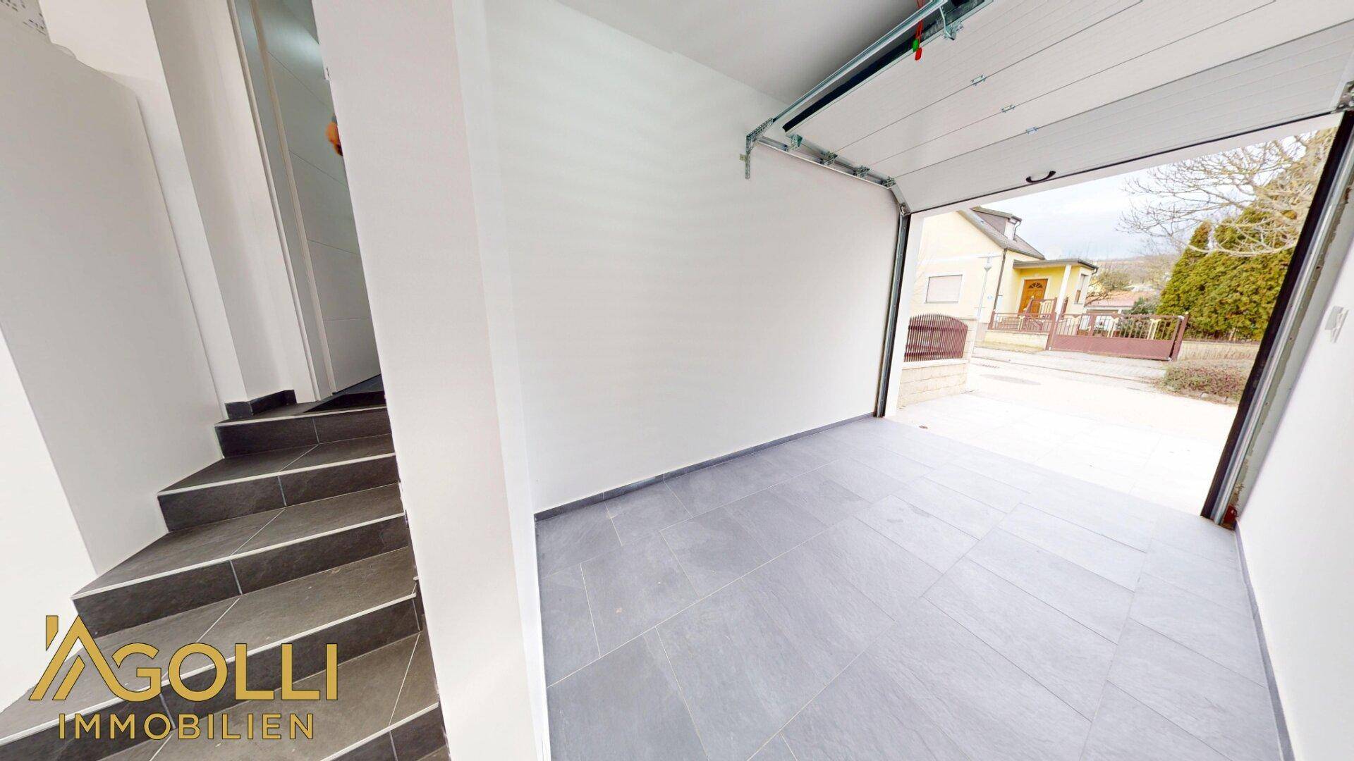 Geräumige Garage mit Fliesenboden und direktem Zugang zum Haus über eine Treppe.