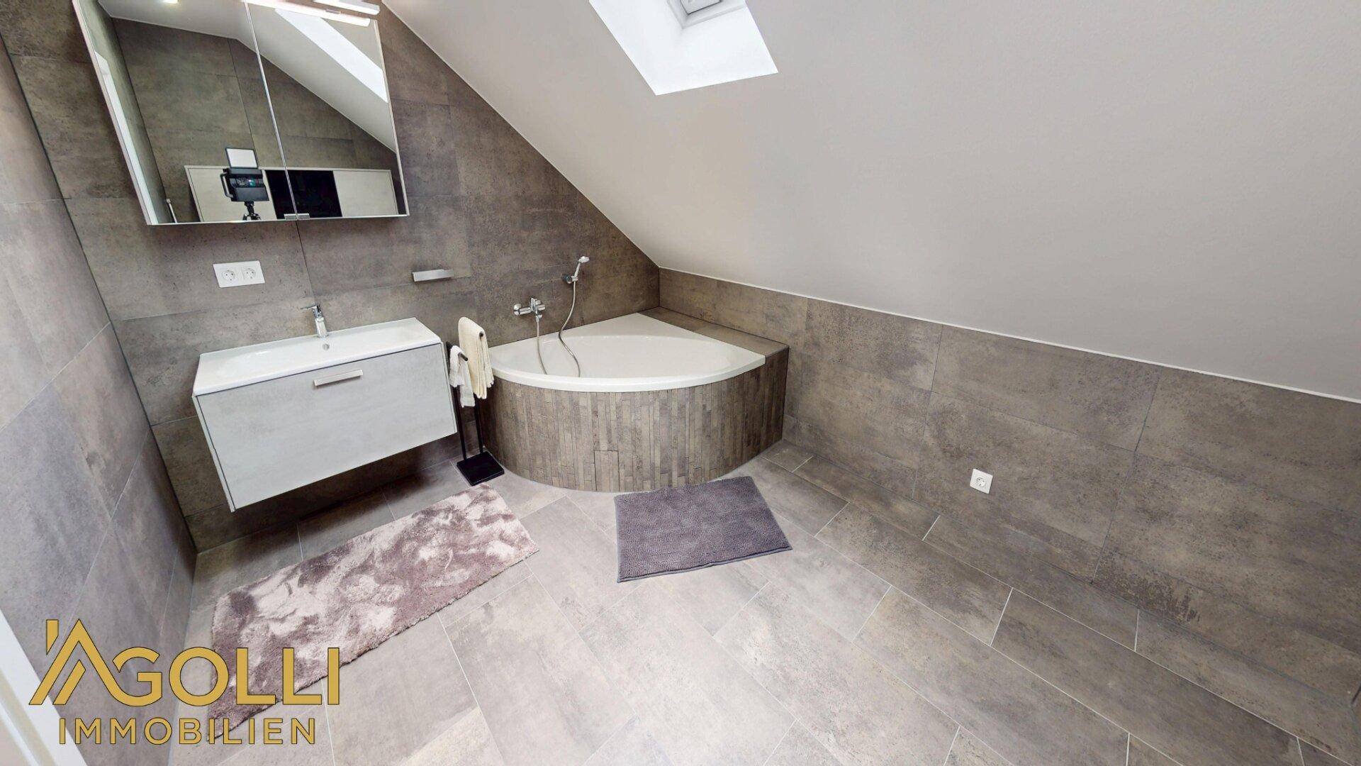 Modernes Badezimmer im Dachgeschoss mit Eckbadewanne, Waschbecken und Dachfenster.