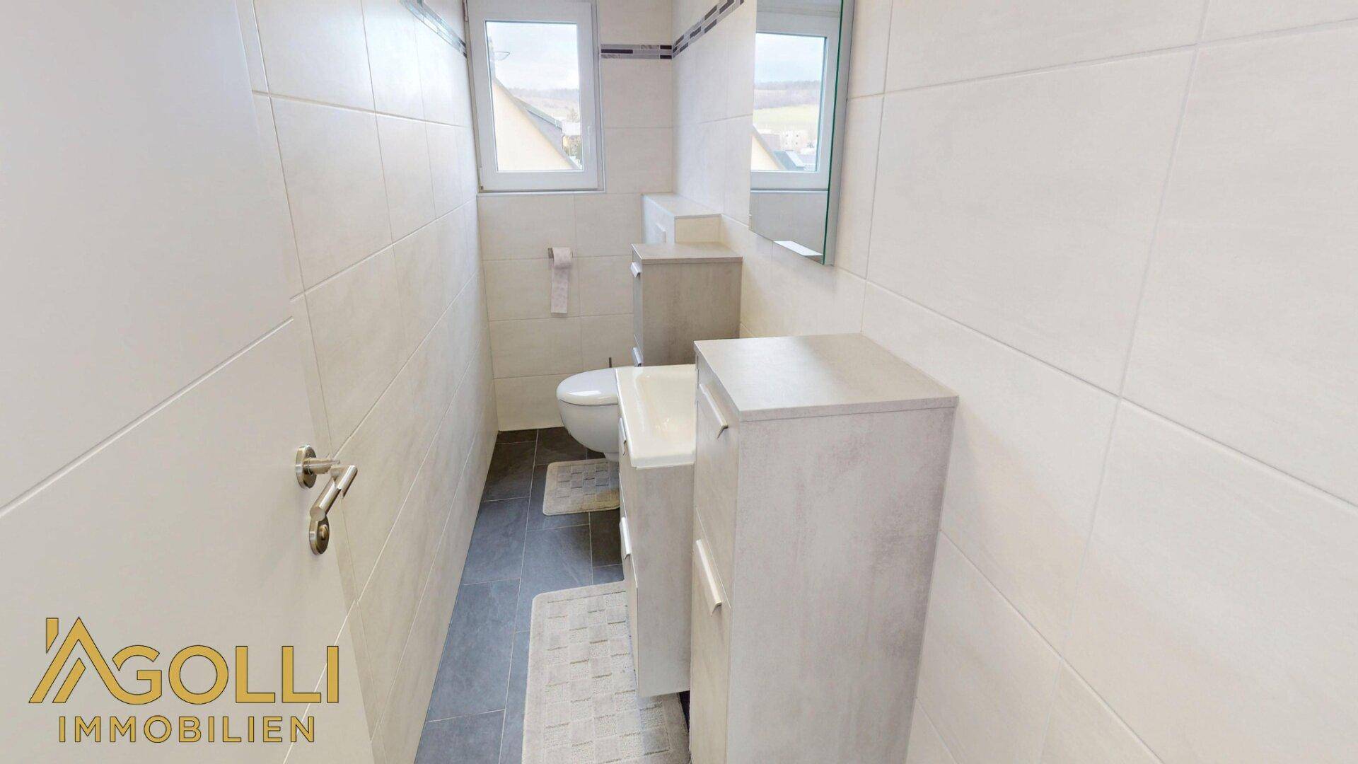 Kleines, hell gefliestes WC mit Waschbecken, Spiegel und Fenster.