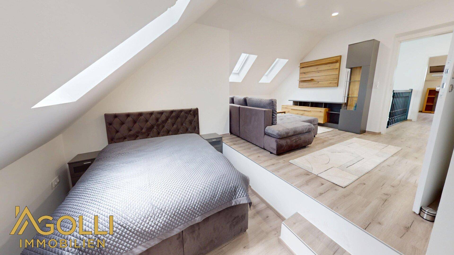 Helles Schlafzimmer im Dachgeschoss mit Doppelbett, Sofa und Dachfenstern.