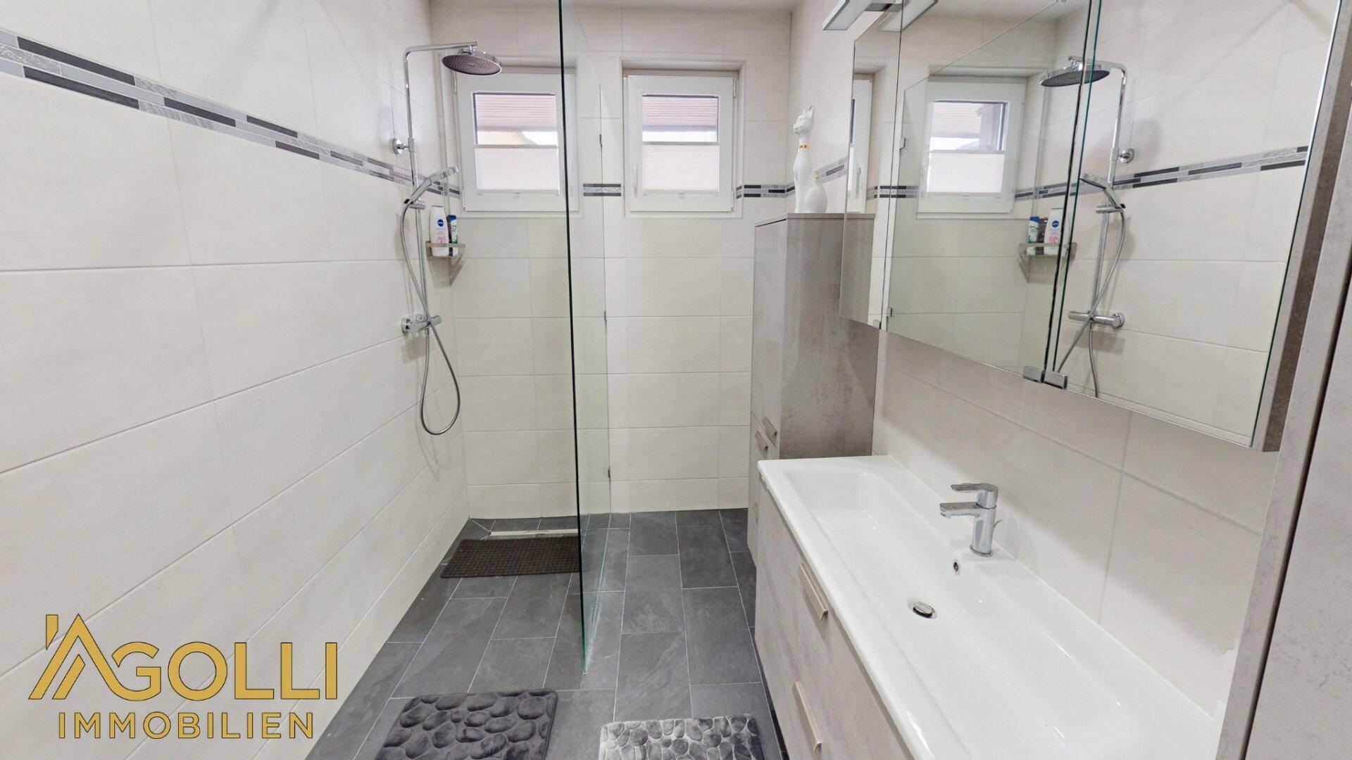 Modernes Badezimmer mit großer begehbarer Dusche, Doppelwaschbecken und Spiegel.