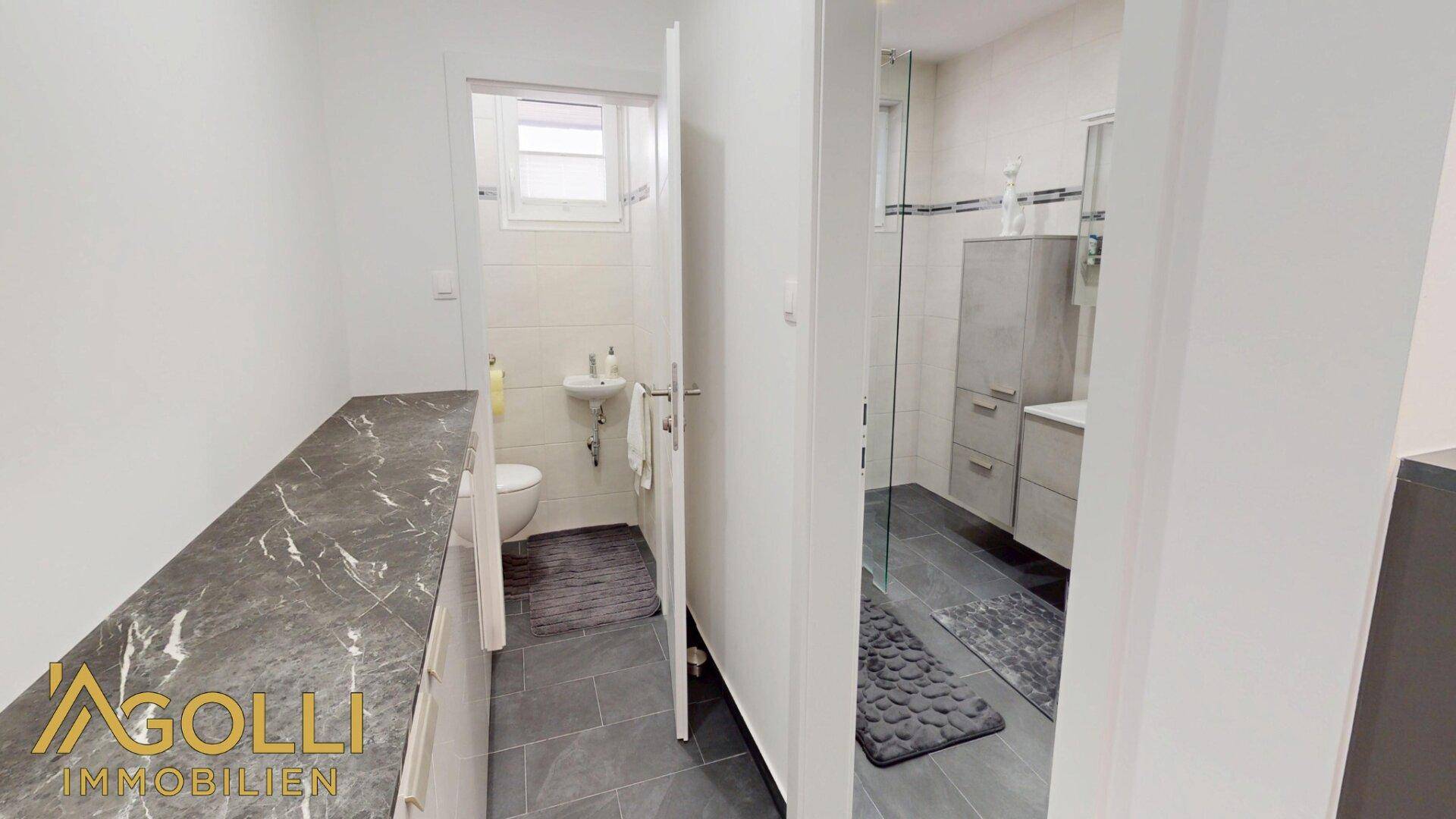 Modernes Badezimmer mit Dusche, WC, Waschbecken und Fenster für Tageslicht.