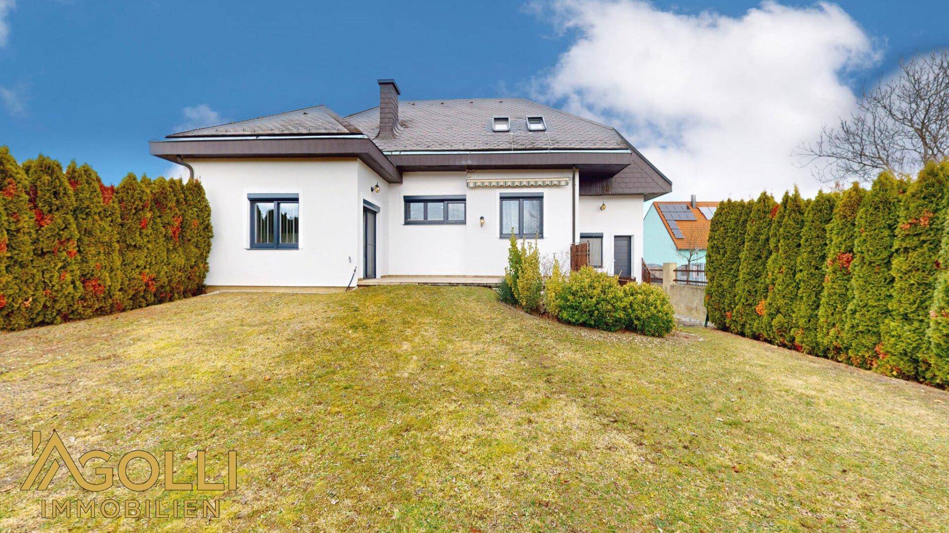 Rückansicht des Hauses mit großem, gepflegtem Garten und hohen Hecken.