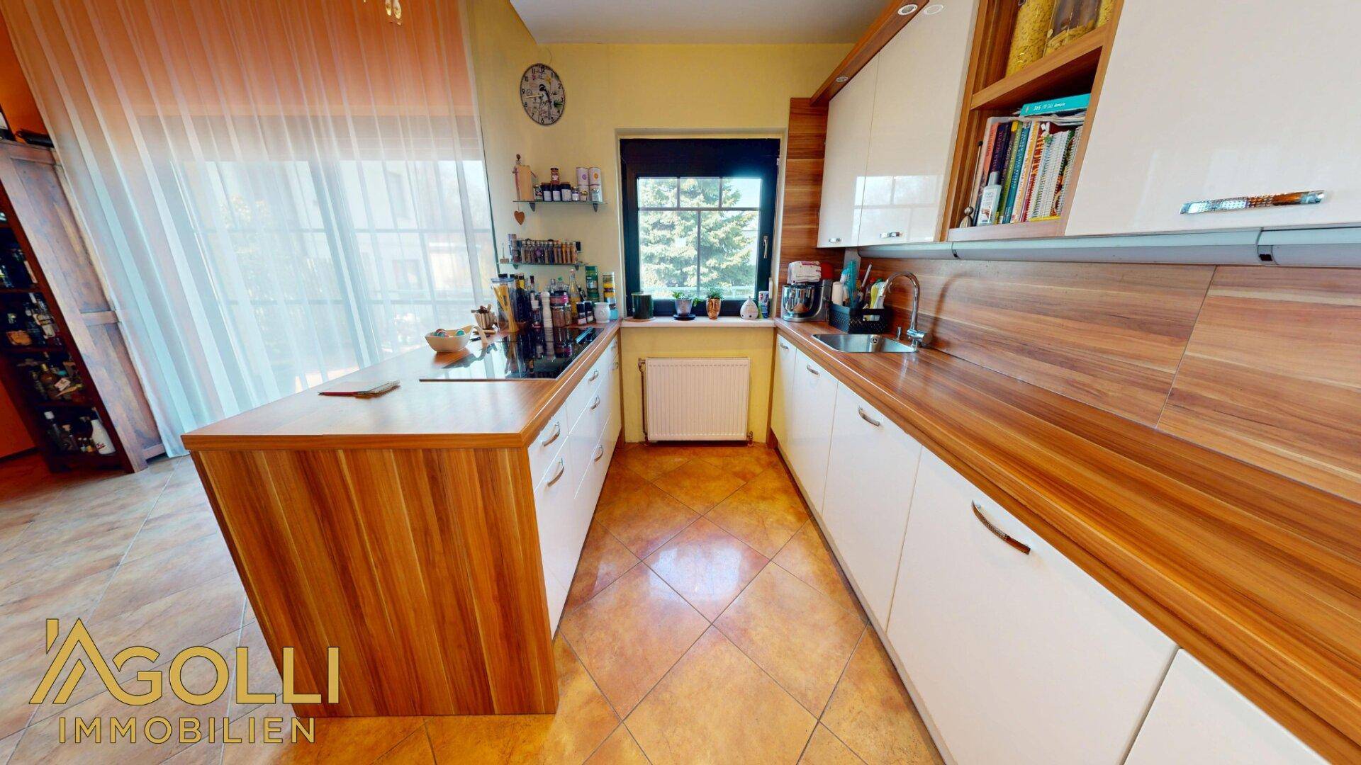 Moderne Küche mit Holz- und weißen Hochglanzfronten, Kochinsel mit Induktionskochfeld und Fliesenboden.