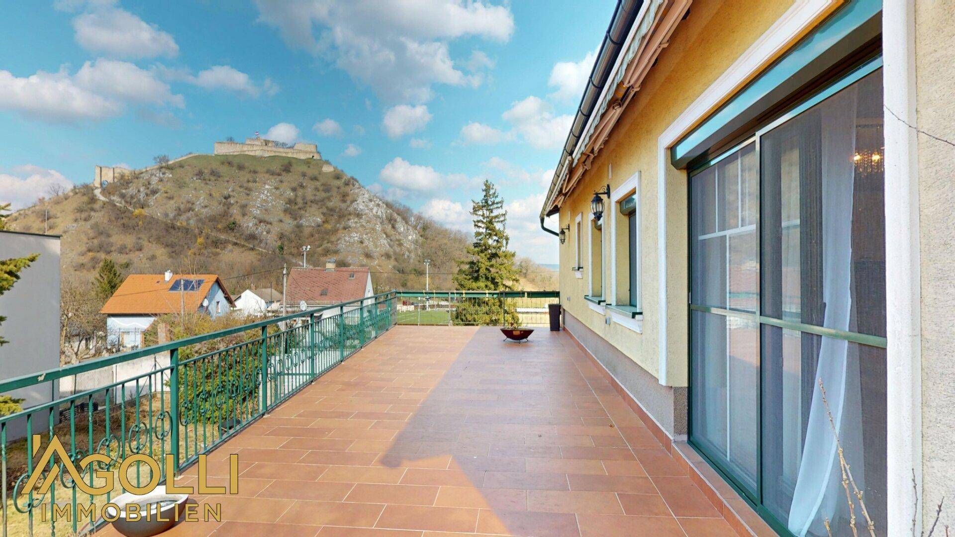 Große Sonnenterrasse mit Fliesenboden, Metallgeländer und weitem Blick auf die Landschaft und Berge.