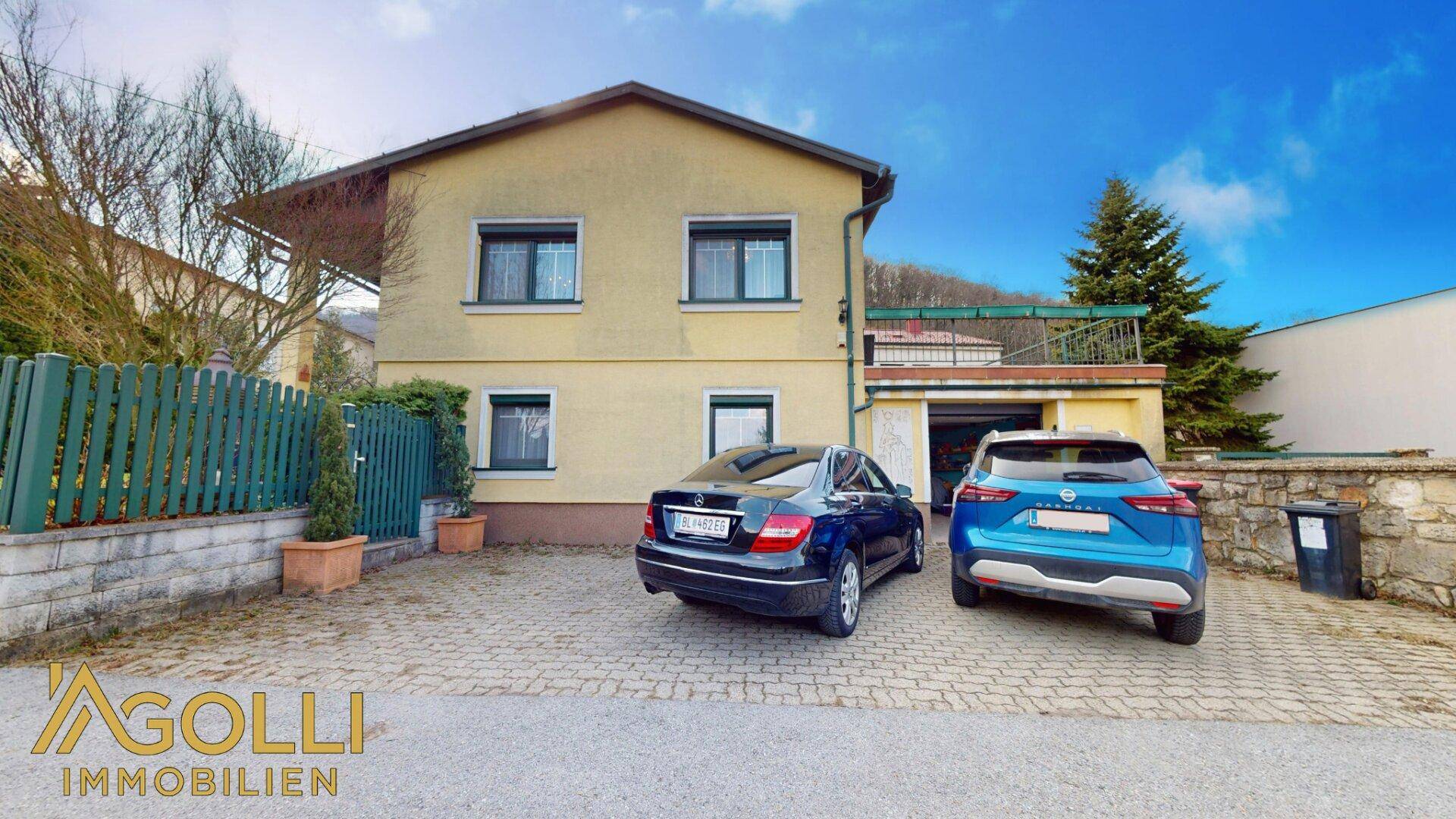 Vorderansicht des Einfamilienhauses mit gepflasterter Auffahrt, zwei geparkten Autos und geschlossenen Rollläden.