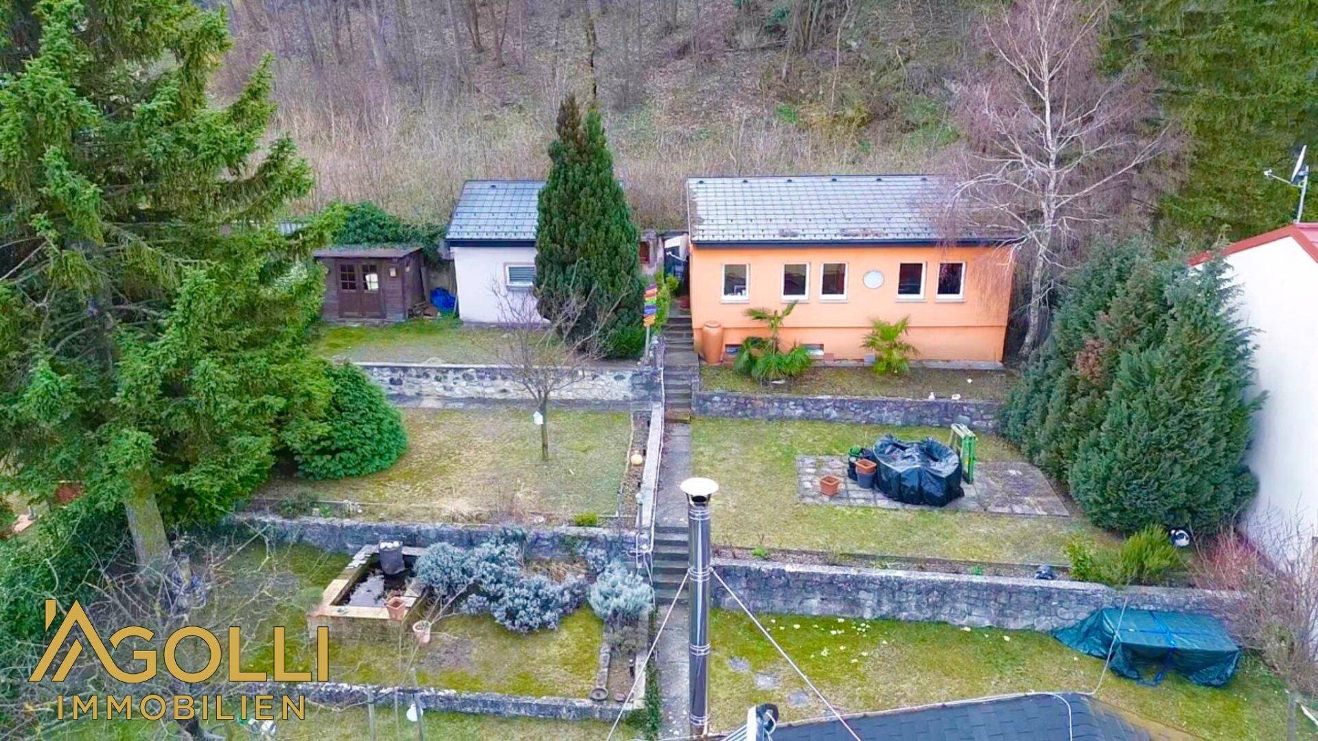 Luftaufnahme des terrassierten Gartens mit Rasenflächen, Bäumen und Nebengebäuden in grüner Umgebung.