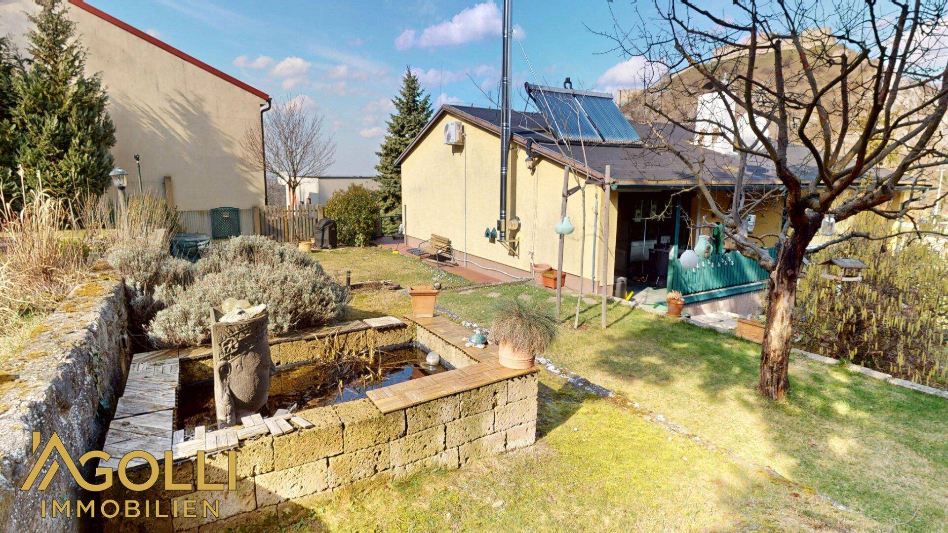 Gepflegter Gartenbereich mit einem dekorativen Teich, Rasenflächen und Solarthermieanlage auf dem Dach.