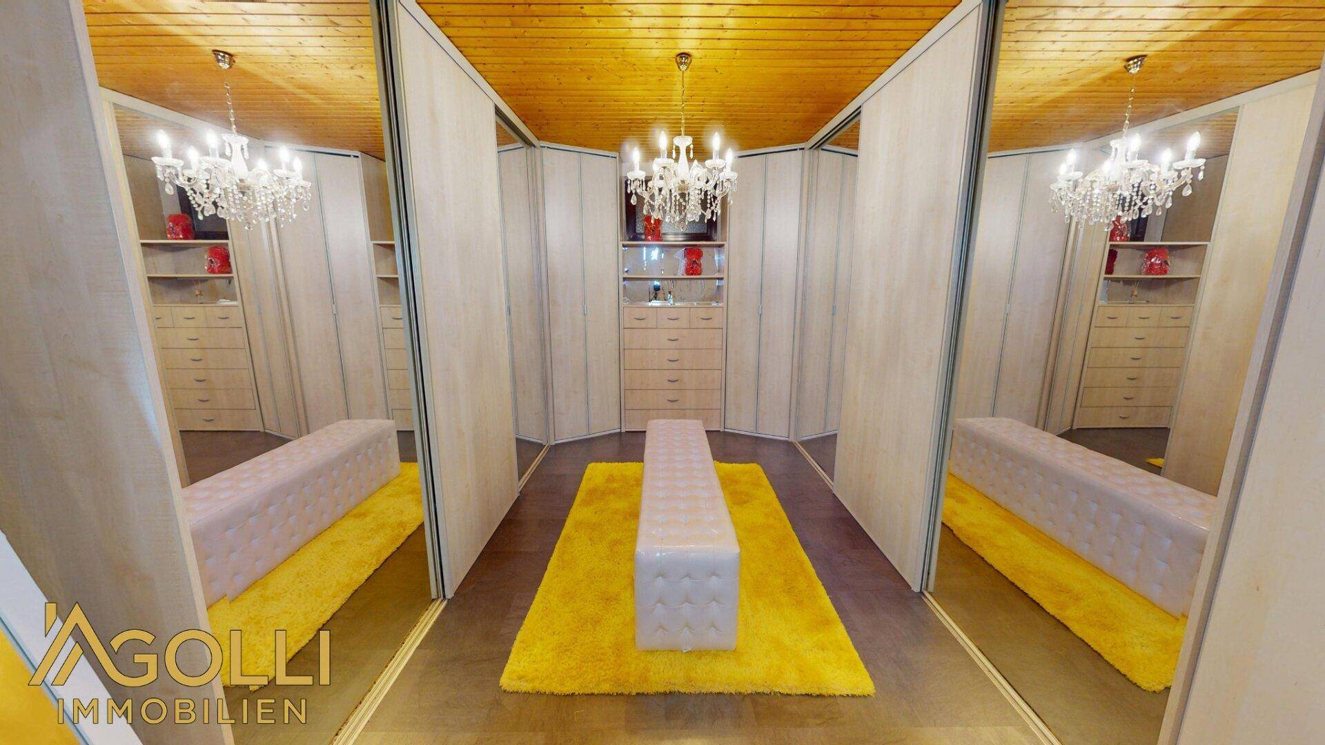 Begehbarer Kleiderschrank mit Spiegeltüren, vielen Schubladen und zentraler Sitzbank für Komfort.