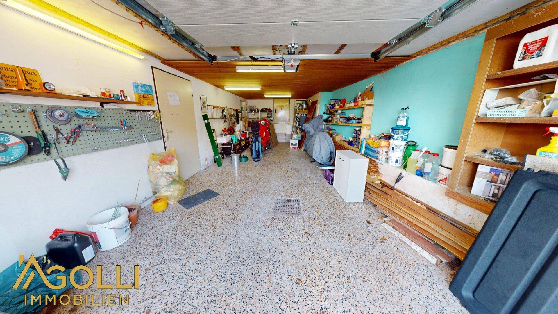 Geräumige Garage, die auch als Werkstatt mit Regalen und Arbeitsflächen genutzt wird.