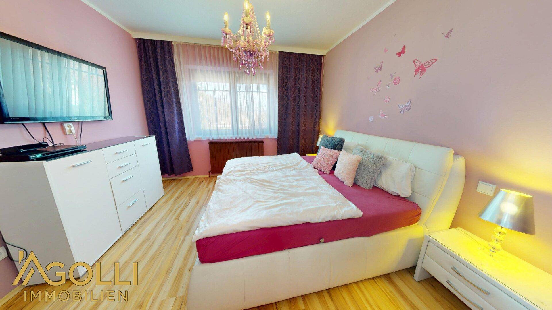 Gemütliches Schlafzimmer mit Doppelbett, rosa Wänden, Kronleuchter und Klimaanlage für angenehme Temperaturen.