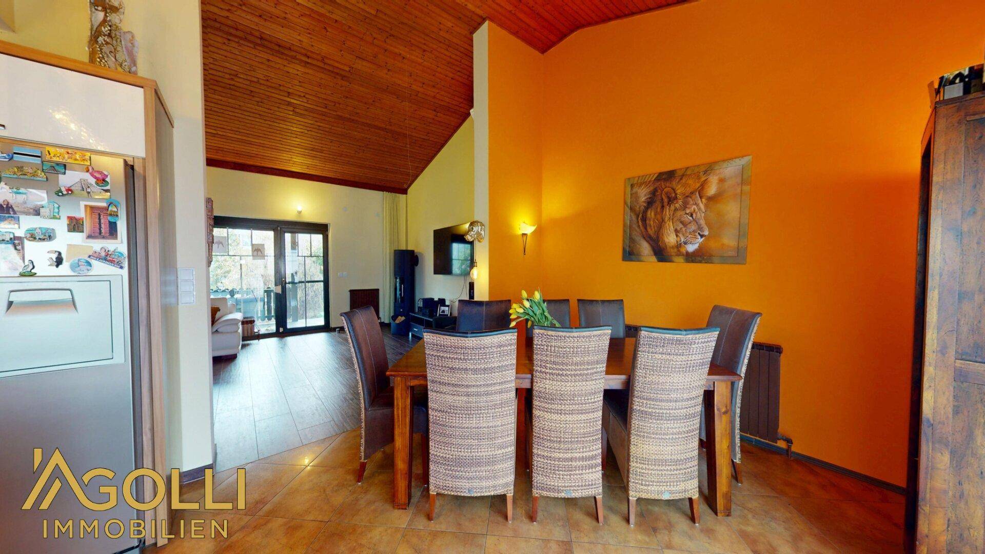 Essbereich mit warmen orangefarbenen Wänden, Holztisch und offenem Blick in den Wohnbereich.