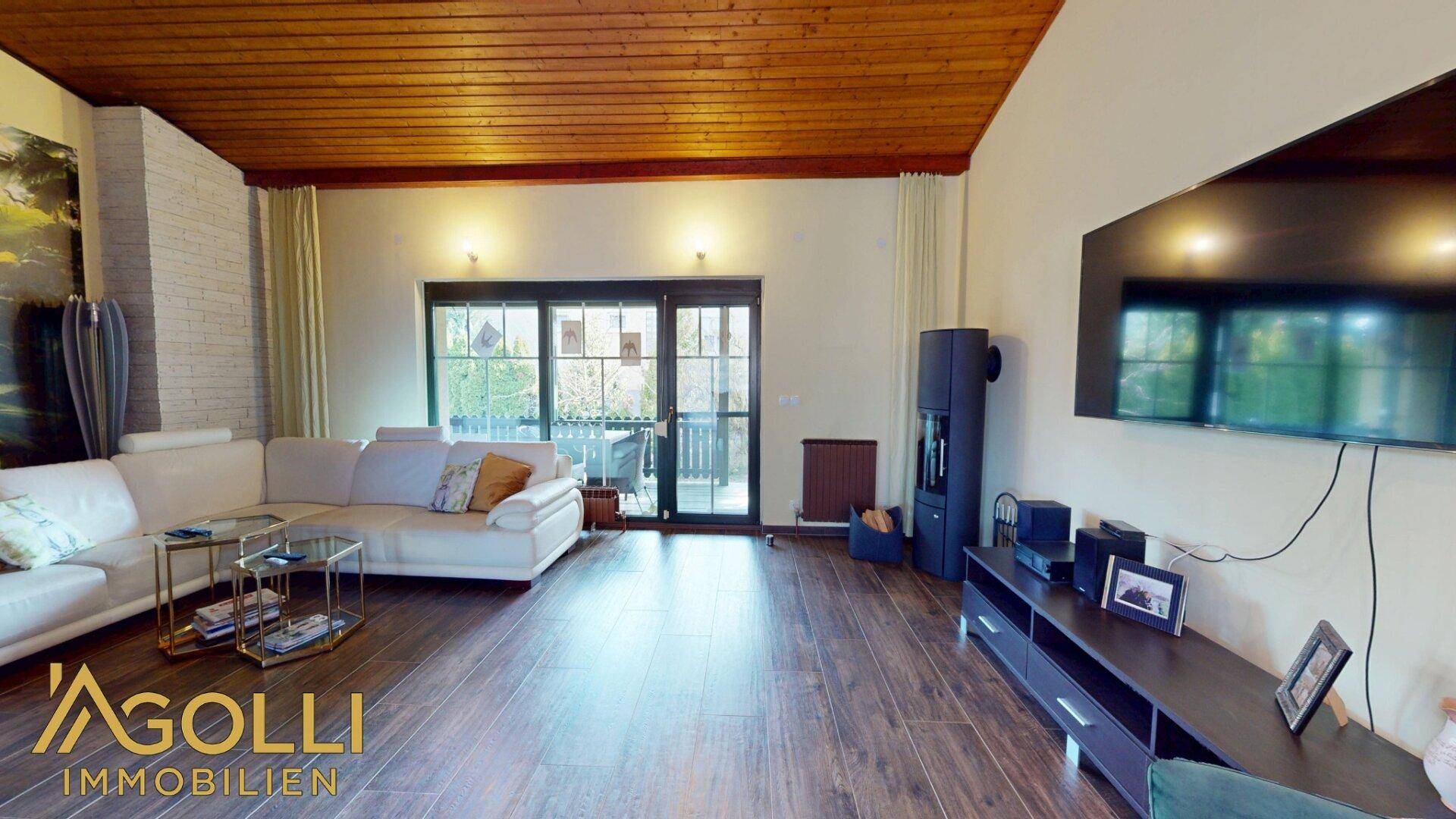Helles Wohnzimmer mit bequemer Couch, Dielenboden, Kaminofen und Zugang zur Terrasse.
