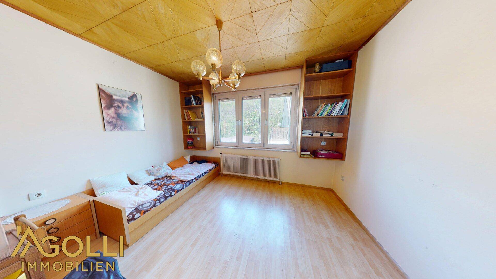 Helles Schlafzimmer mit Einzelbett, eingebauten Bücherregalen und Holzdecke.
