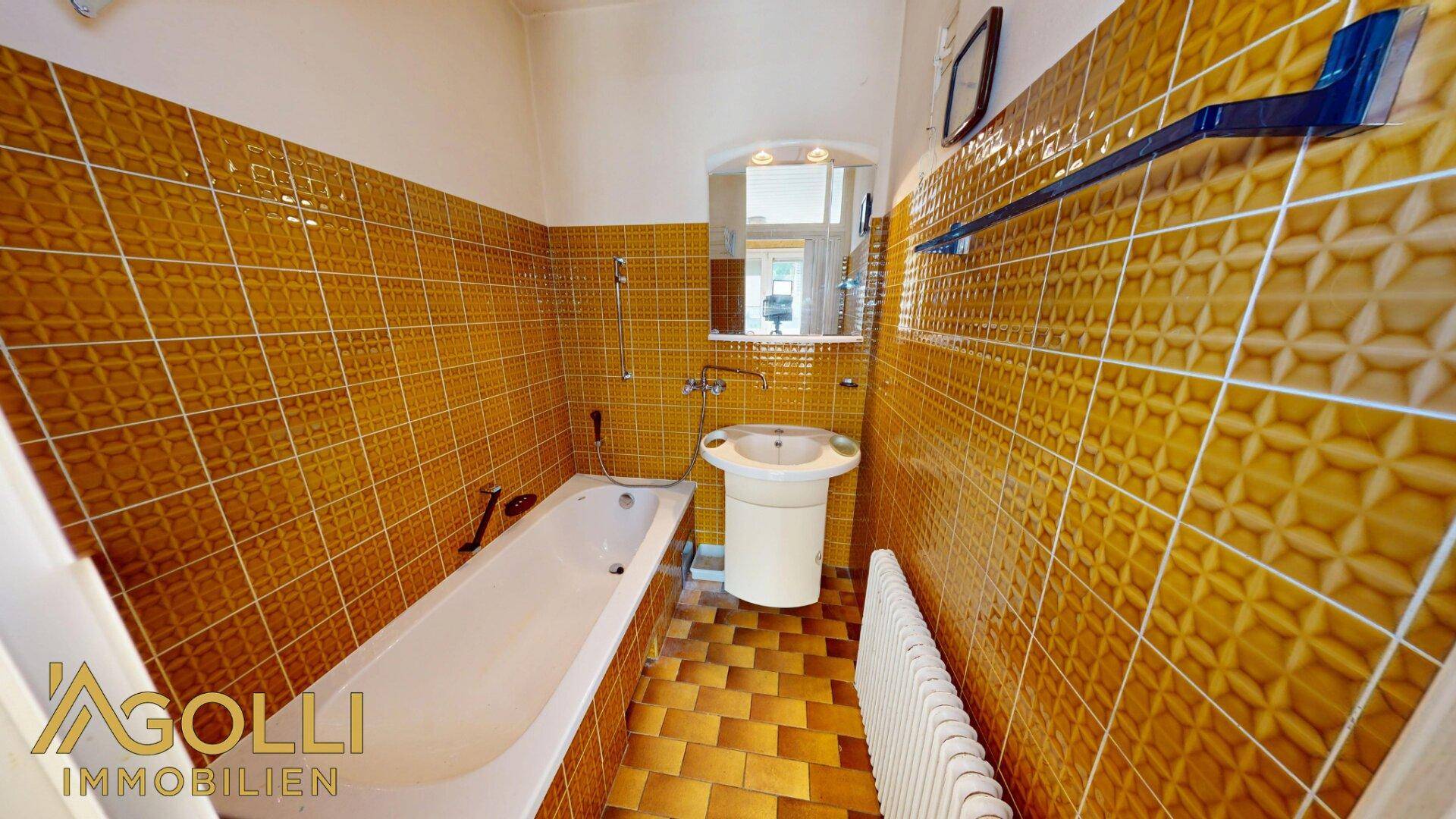 Badezimmer mit gemusterten orange-braunen Fliesen, Badewanne und Einzelwaschbecken.
