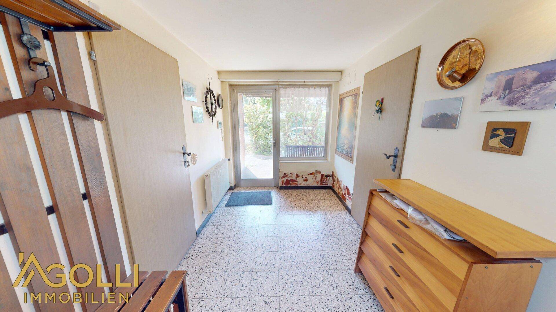 Eingangsbereich mit Terrazzoboden, Garderobe und einer Glastür zum Außenbereich.