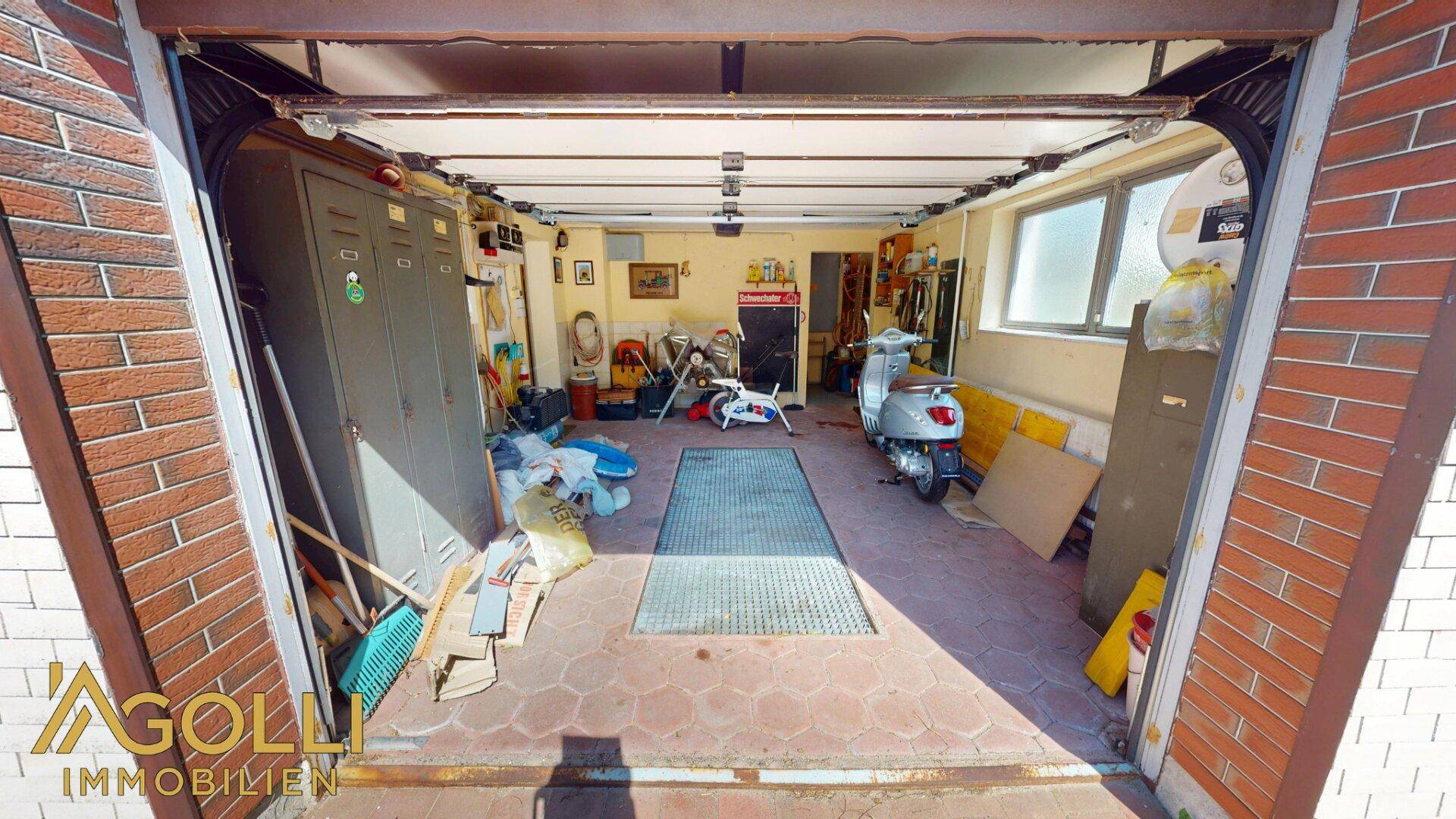 Blick in die Garage mit Werkstattbereich, Lagerung und einem Roller.
