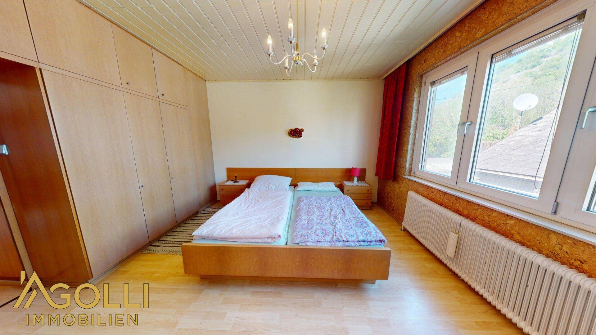 Schlafzimmer mit Doppelbett, Einbauschränken und einem Fenster, das Tageslicht hereinlässt.