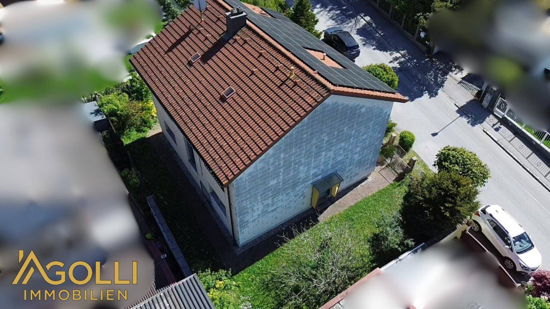 Luftaufnahme des Hauses von der Seite mit Ziegeldach und angrenzender Straße.