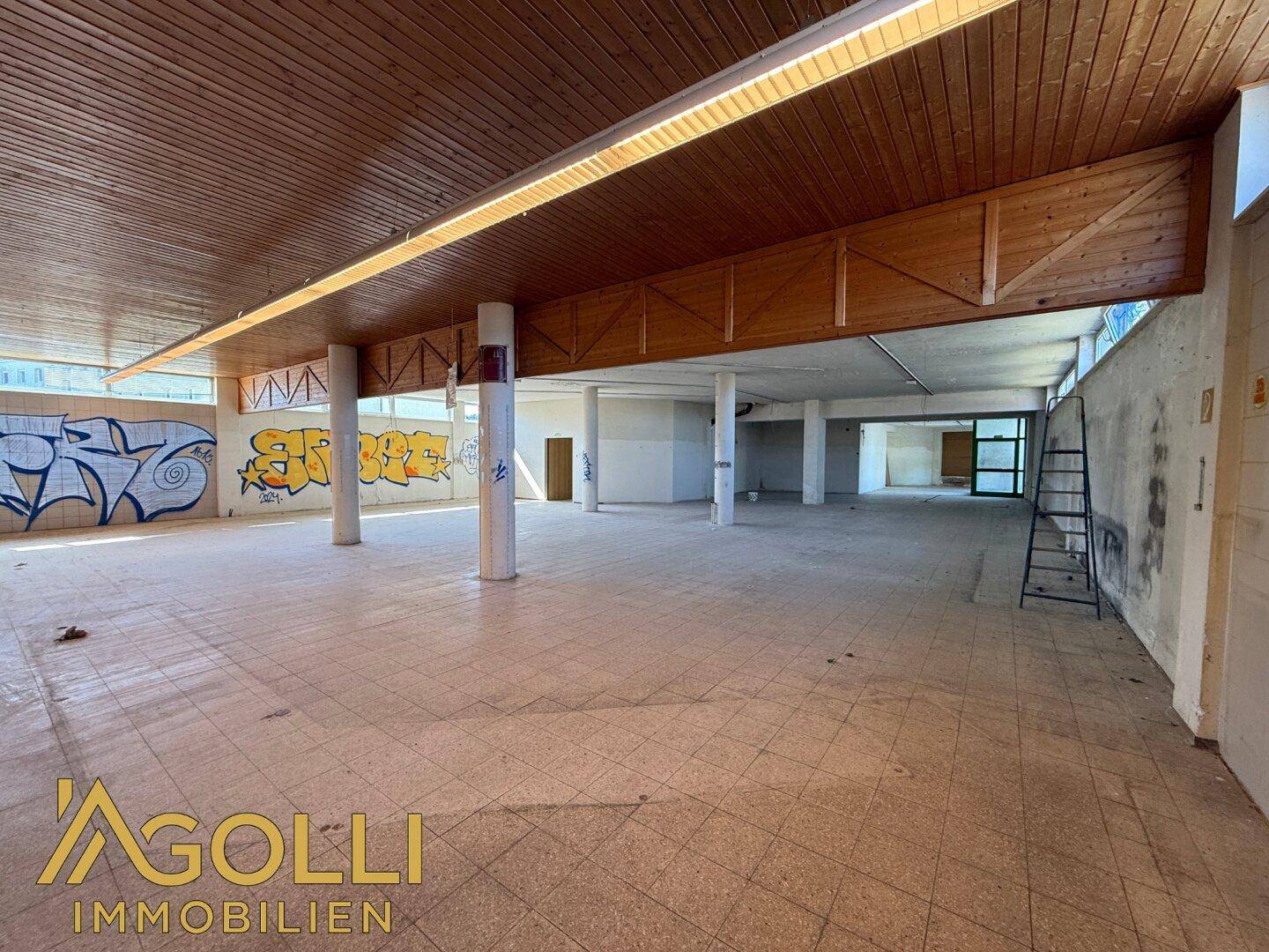 Weitläufiger Innenraum mit Fliesenboden, Holzdecke und Graffiti an den Wänden, ideal für kreative Projekte.