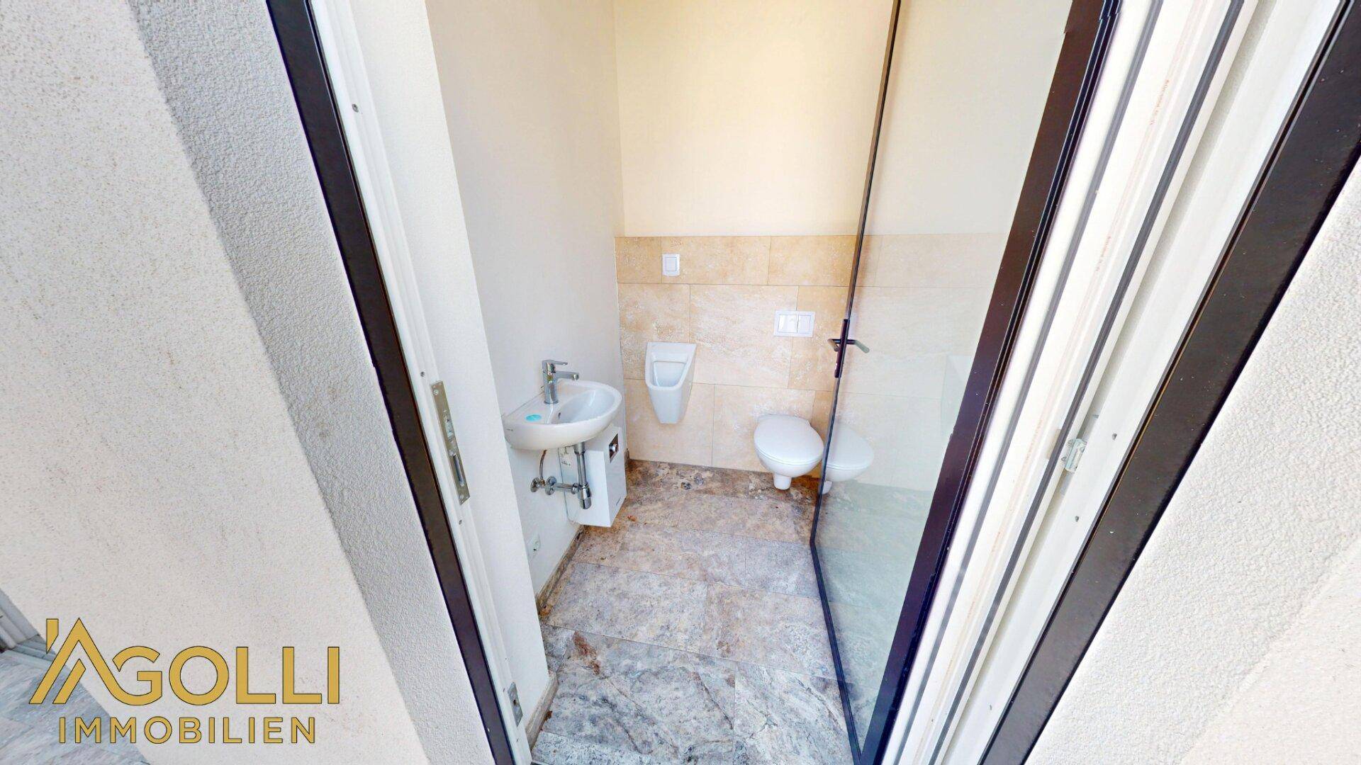 Kleines Gäste-WC mit Urinal, Waschbecken und Wand-WC, durch Glastür abgetrennt.