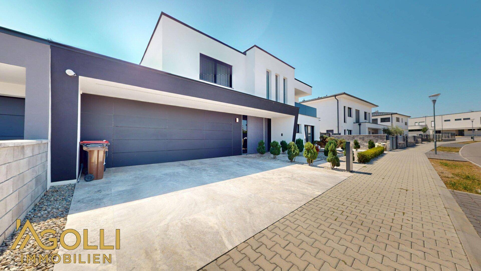 Seitenansicht der modernen Villa mit breiter Garageneinfahrt und schlichter Gestaltung.