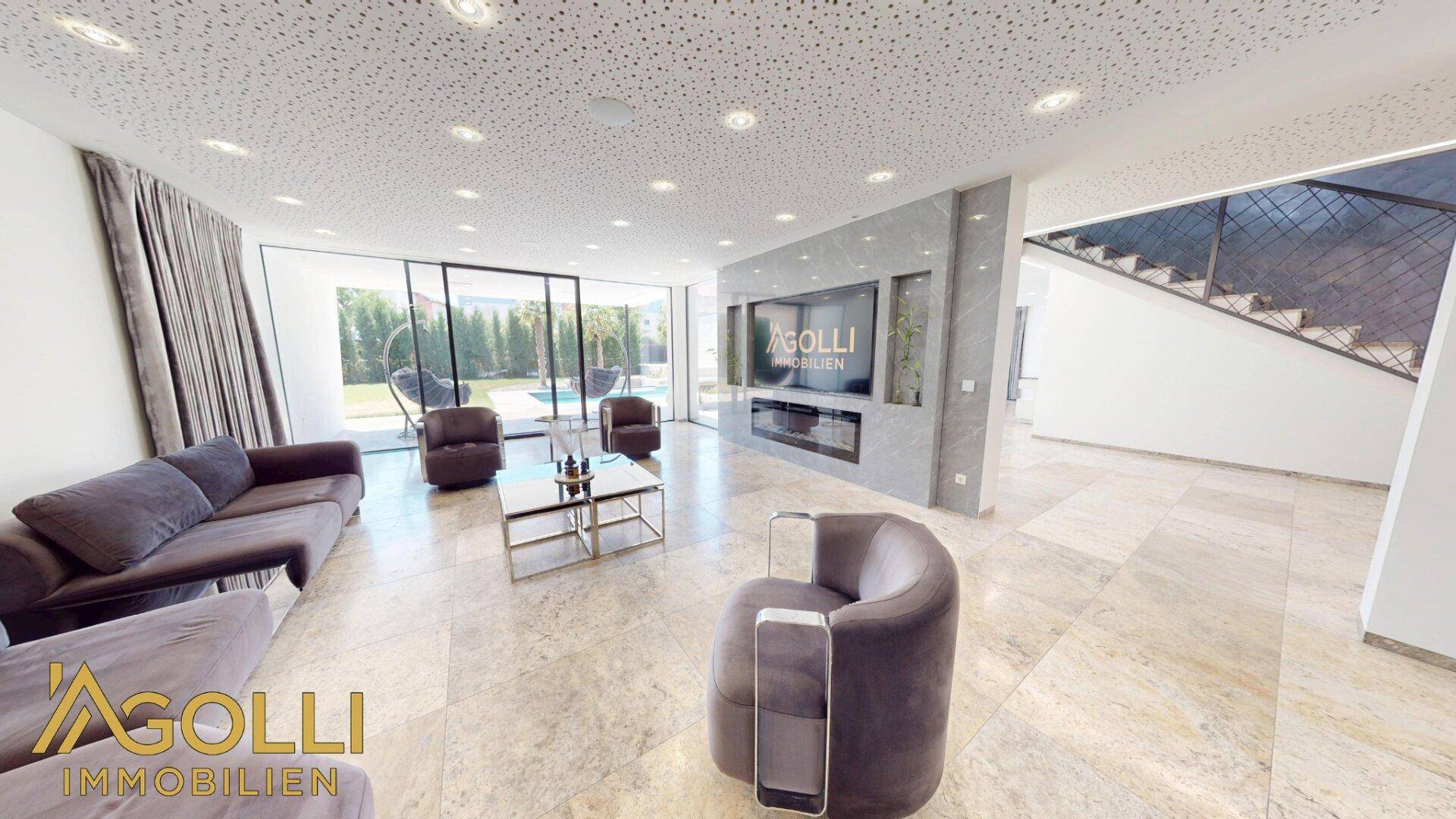 Helles Wohnzimmer mit Blick auf den Poolbereich und offener Treppe zum Obergeschoss.