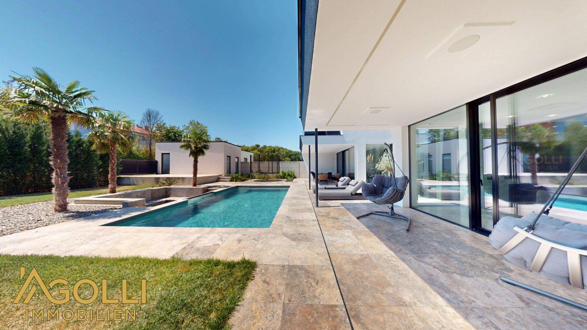 Seitliche Ansicht des Pools und der Terrasse mit Blick auf die moderne Hausfassade.