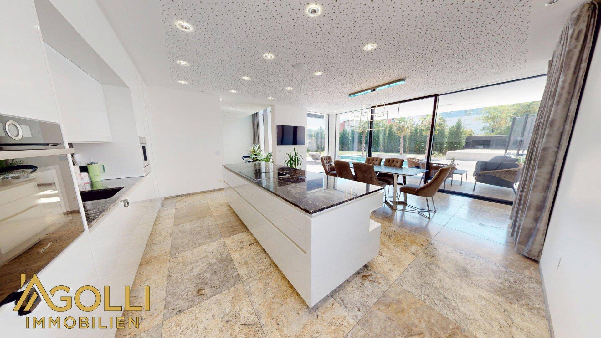 Moderne Küche mit Kochinsel, Essbereich und Zugang zur Terrasse mit Poolblick.