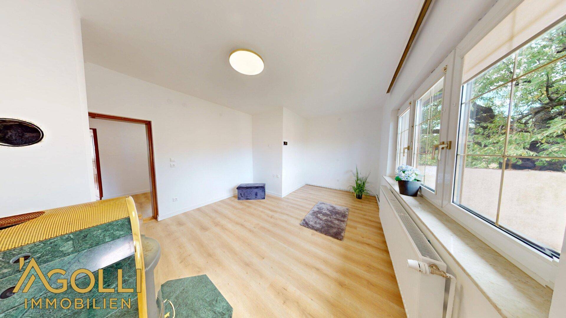 Geräumiges Wohnzimmer mit hellem Laminatboden und Blick ins Grüne durch große Fenster.