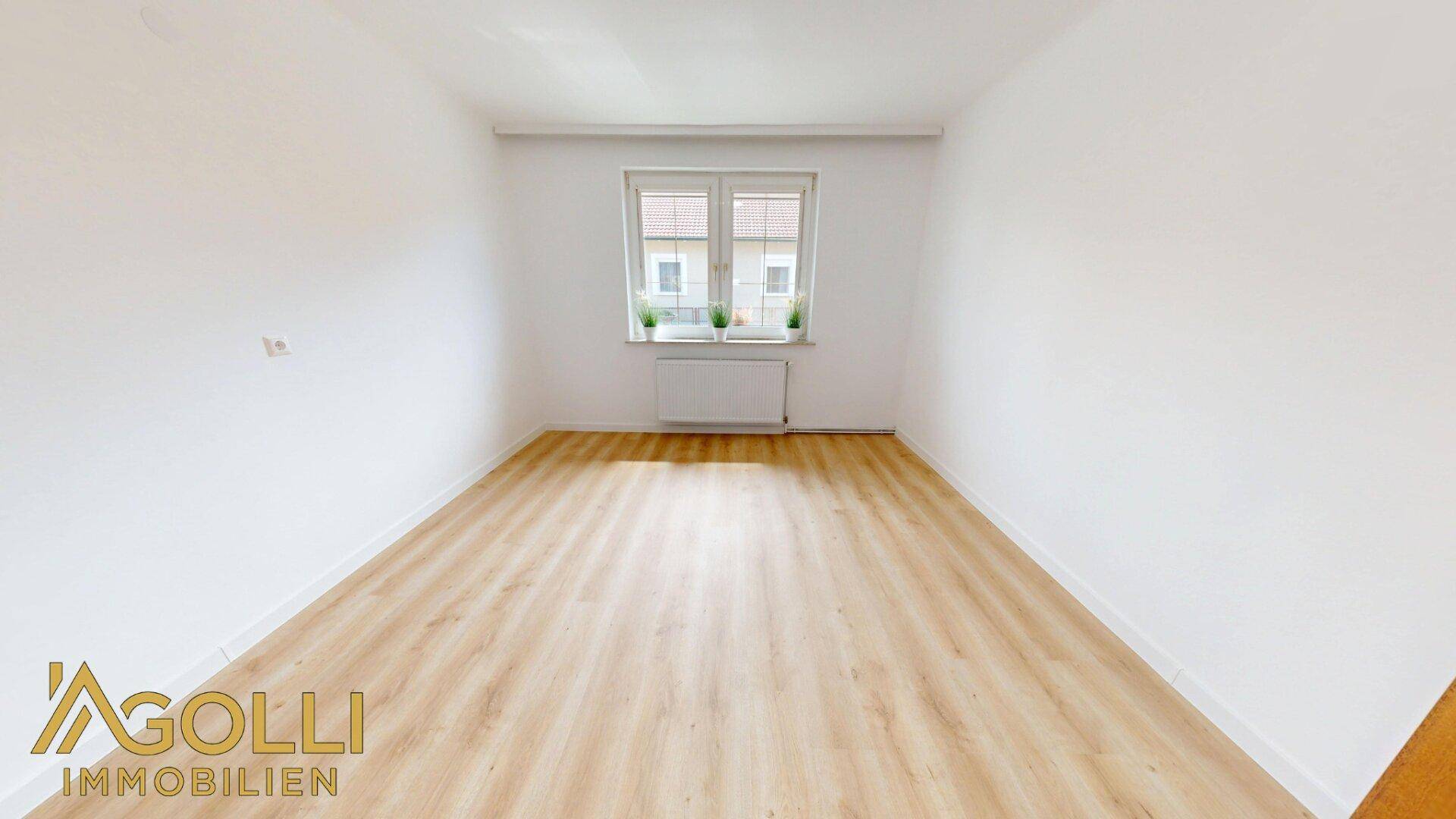 Helles Schlafzimmer mit Laminatboden und einem Fenster, das viel Tageslicht hereinlässt.