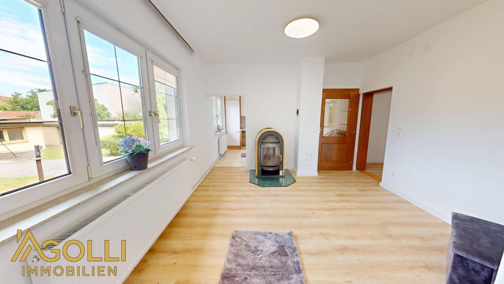 Helles Wohnzimmer mit Laminatboden, großem Fenster und einem gemütlichen Holzofen.