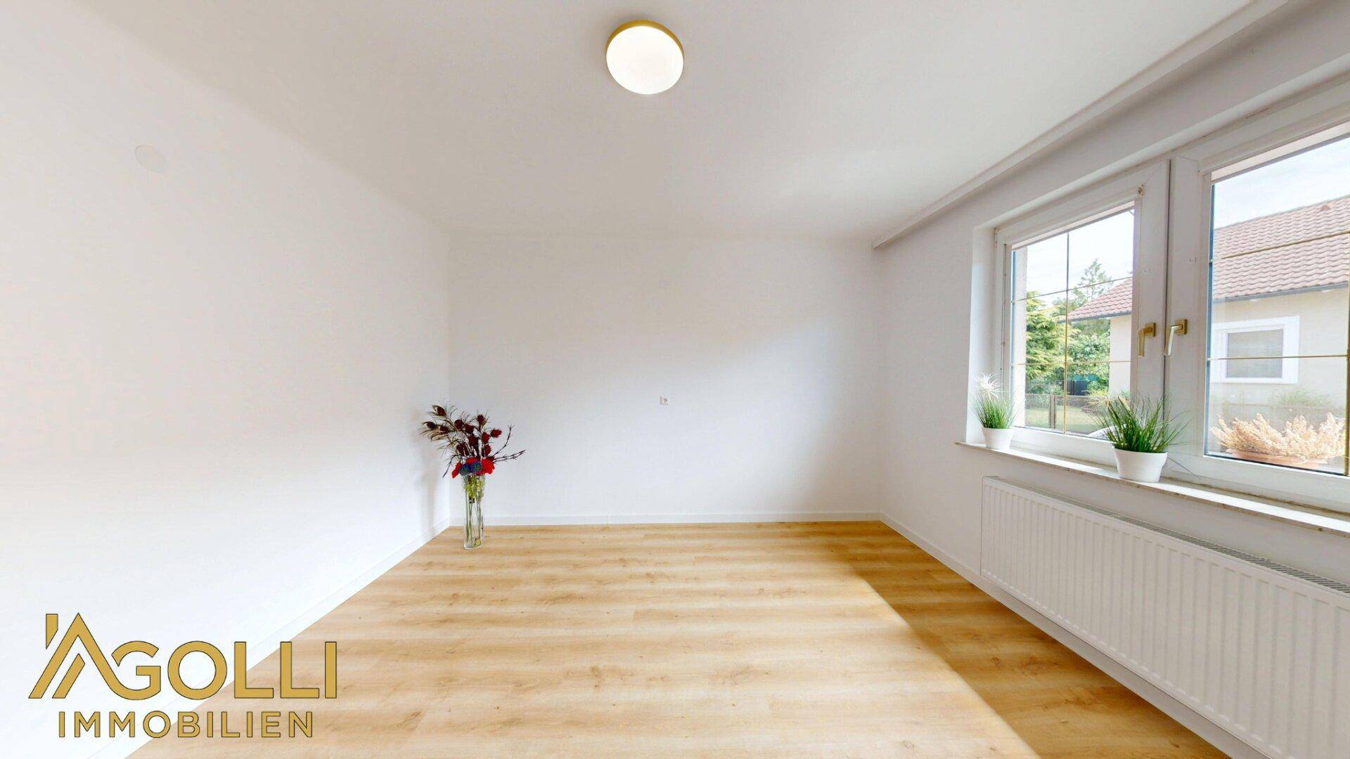 Geräumiges Zimmer mit hellem Laminatboden und großen Fenstern für natürliche Belichtung.